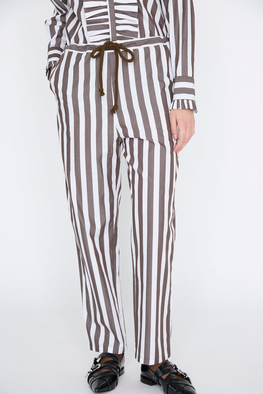 A model wears Les Prairies De Paris's Pantalon Nicolo in Marron, featuring organic cotton brown and white vertical stripes with a tied waistband, paired with sleek black shoes.