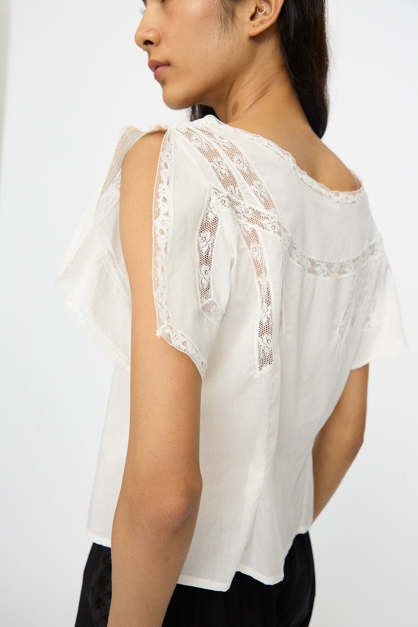 A person models the Loretta Caponi Angela Top in Sunrise, a lightweight cotton piece with lace-detailed sleeves and back, shown from the side and back against a plain background.
