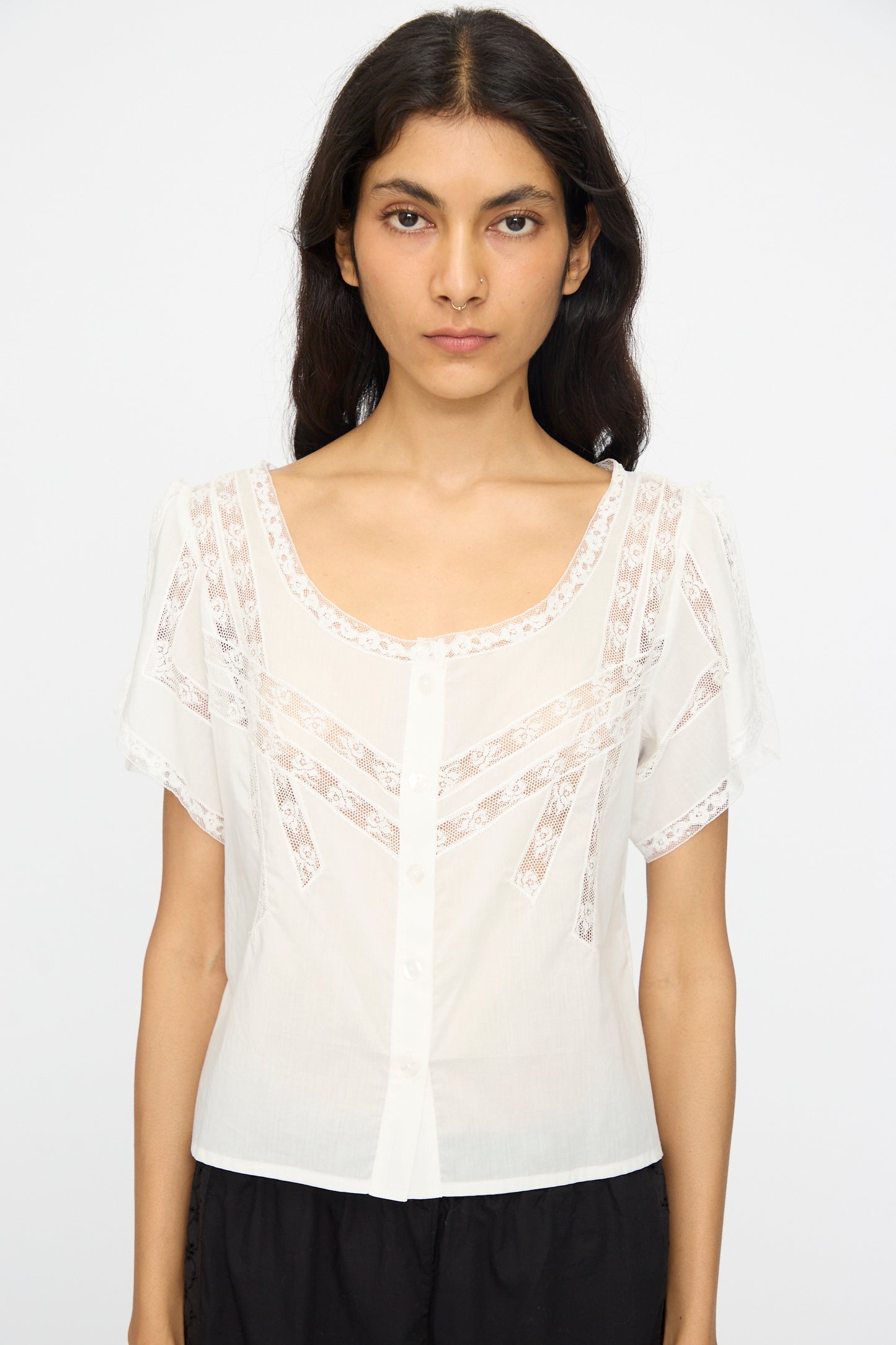 A woman wearing the Loretta Caponi Angela Top in Sunrise, a lightweight cotton piece with lace details and front buttons, made in Italy, stands against a plain white background.