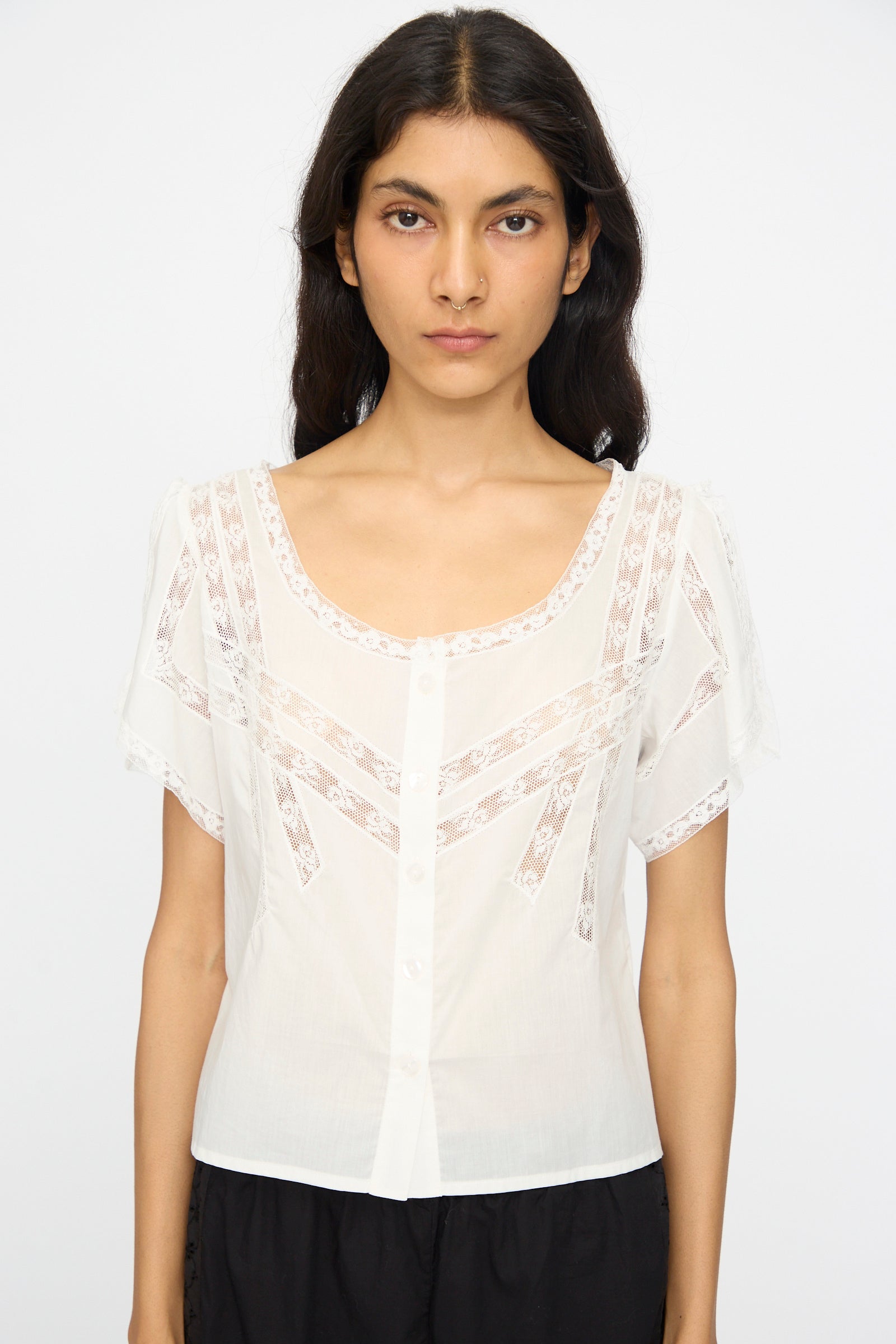 A woman wearing the Loretta Caponi Angela Top in Sunrise, a lightweight cotton piece with lace details and front buttons, made in Italy, stands against a plain white background.