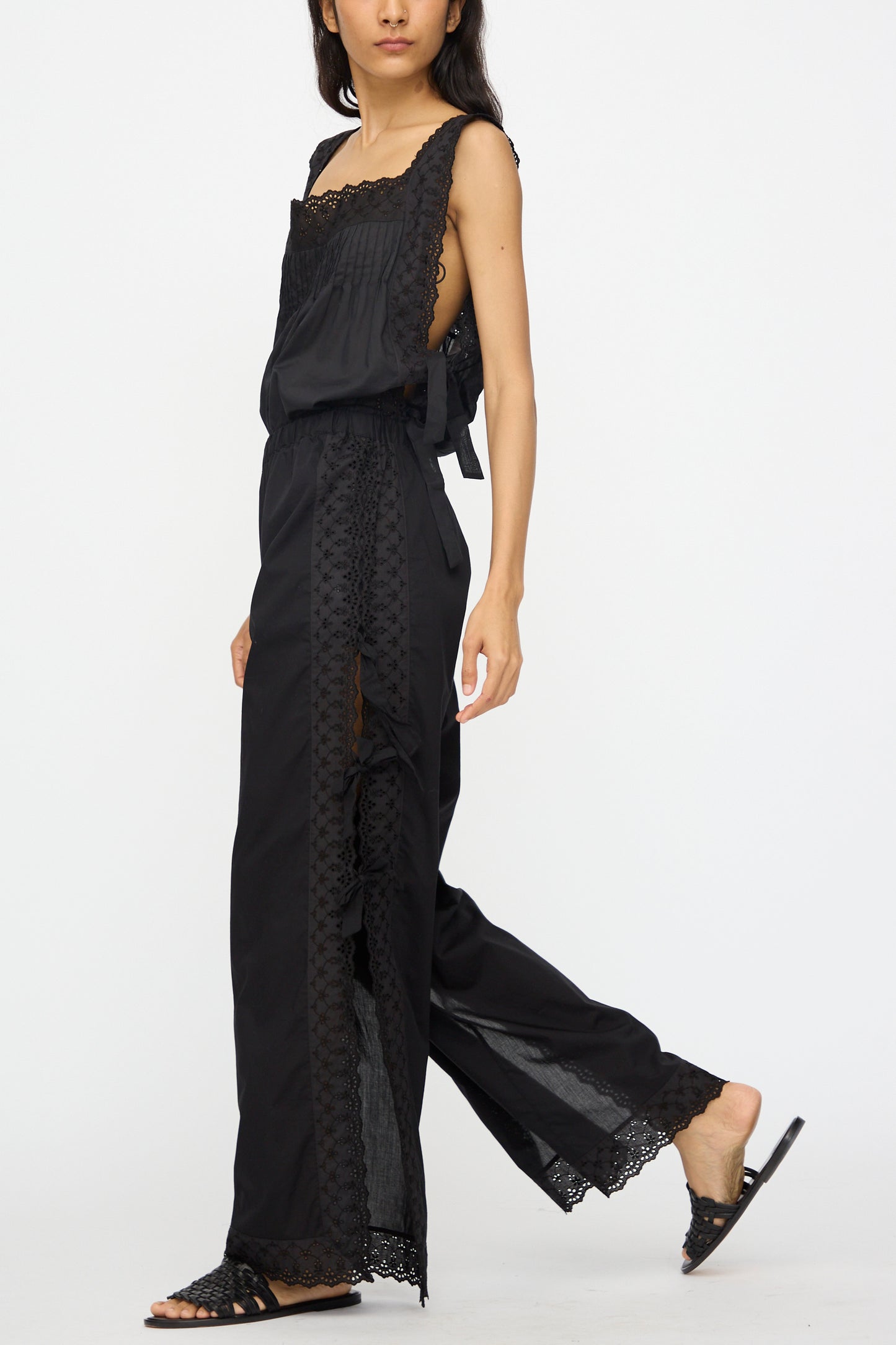 A woman showcases the Loretta Caponi Clarissa Trousers in Nero—high waisted and stylish—paired with black flat sandals, walking against a plain white background.