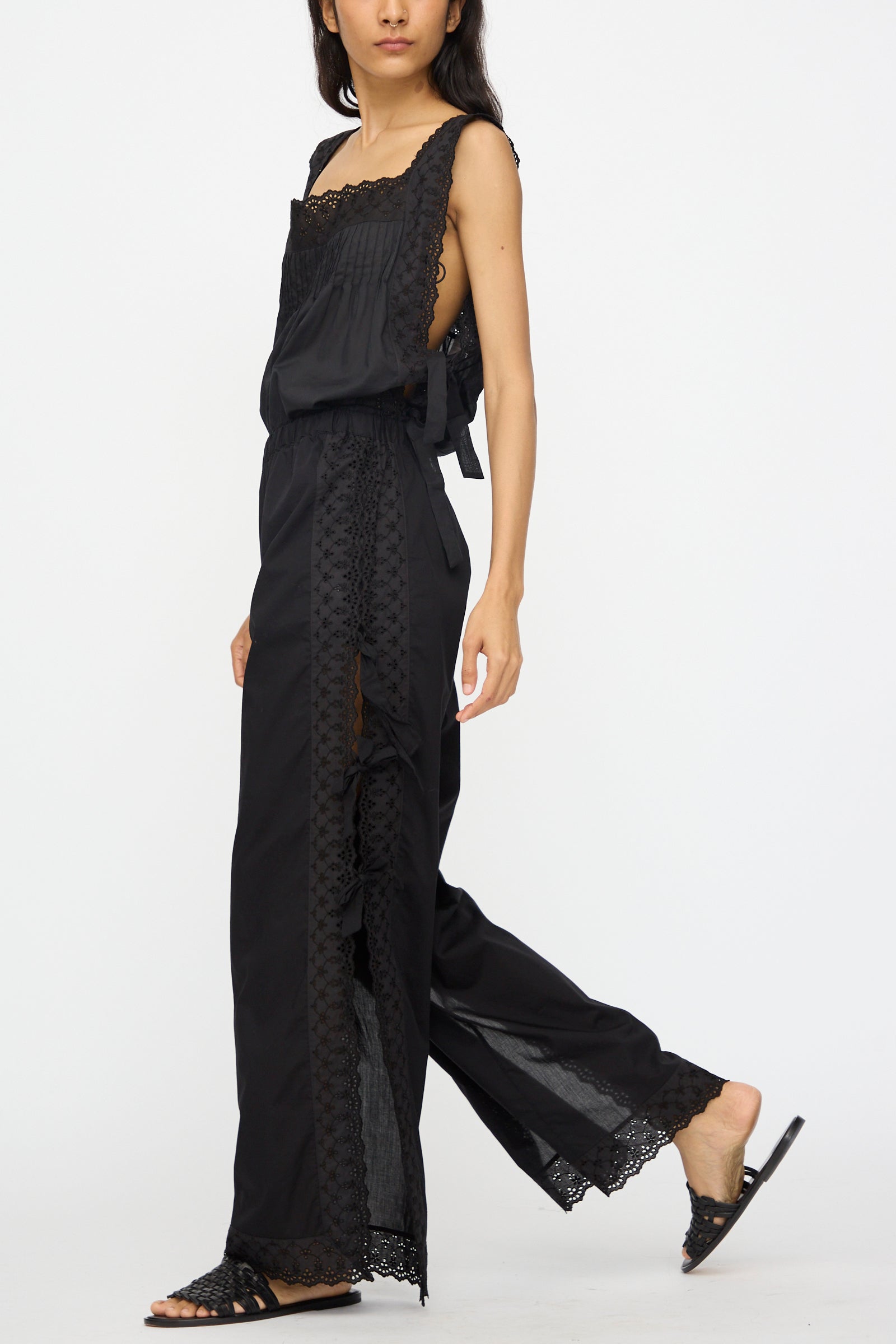 A woman showcases the Loretta Caponi Clarissa Trousers in Nero—high waisted and stylish—paired with black flat sandals, walking against a plain white background.