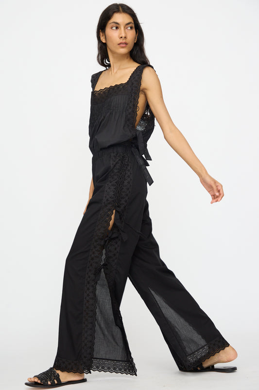 A person walks forward against a plain white background wearing Loretta Caponi's Clarissa Trousers in Nero, featuring a high-waisted, wide-leg silhouette with side slits.