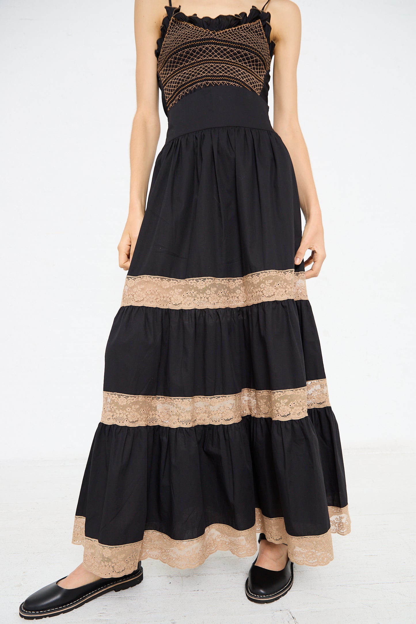 A person wearing a Cotton Violetta Maxi Skirt in Black by Loretta Caponi with intricate lace details and black slip-on shoes, standing on a light-colored floor. The high-waist design adds a flattering touch to the elegant outfit.