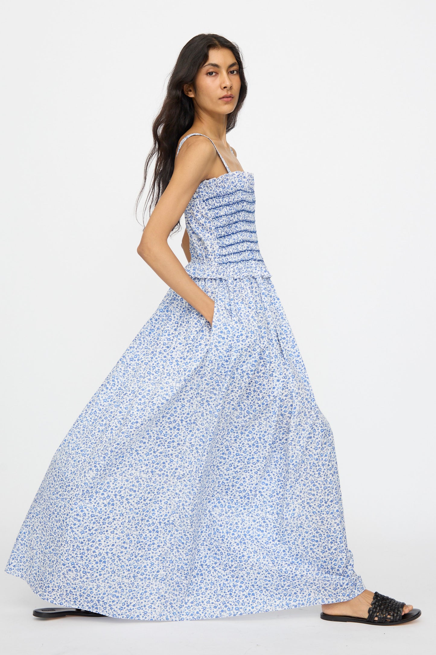 A person wearing the Loretta Caponi Ombretta Dress in Marina Grande—a long blue and white floral cotton maxi dress with thin straps, ruched fitted bodice, and flowing skirt—exudes timeless elegance made in Italy.