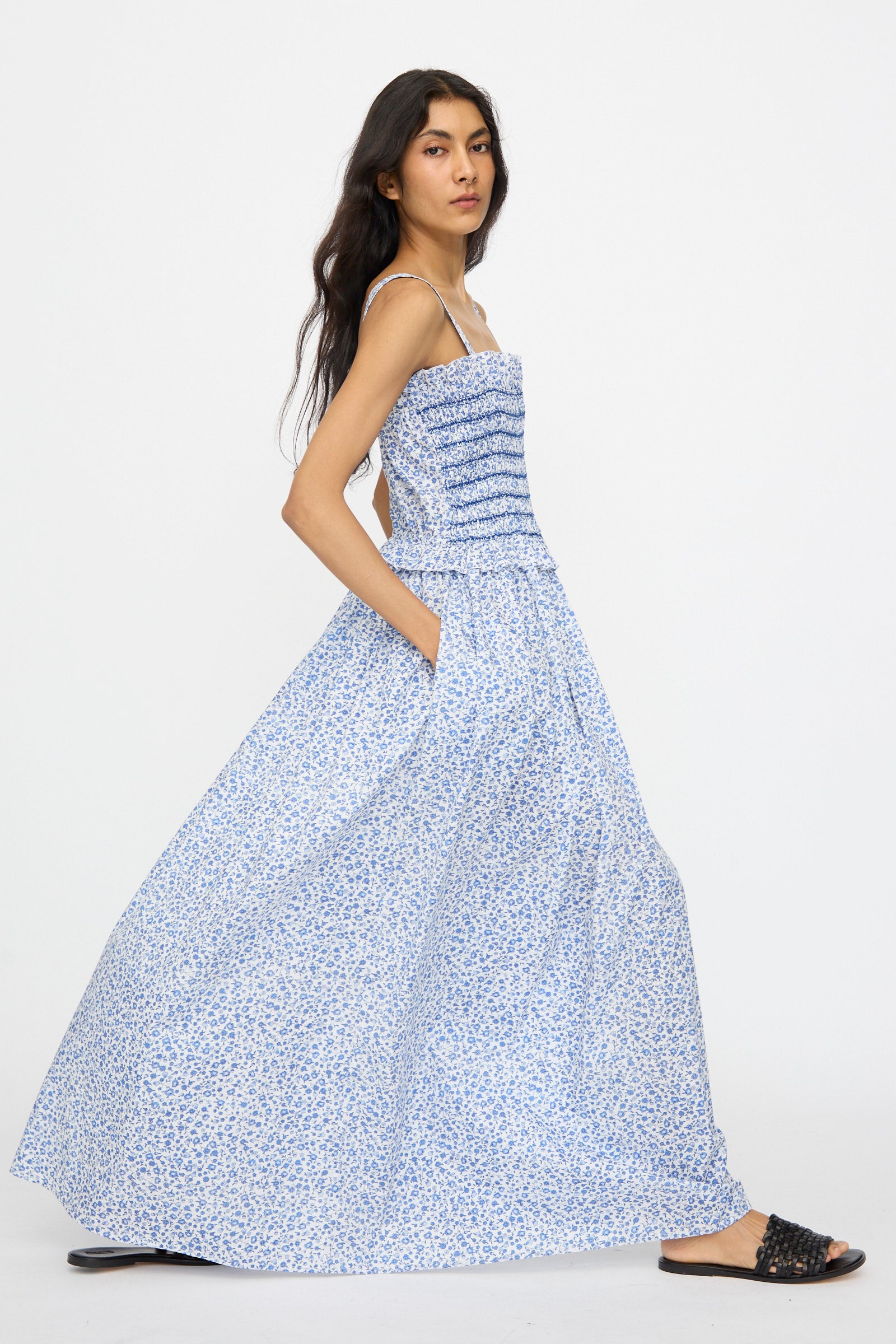 A person wearing the Loretta Caponi Ombretta Dress in Marina Grande—a long blue and white floral cotton maxi dress with thin straps, ruched fitted bodice, and flowing skirt—exudes timeless elegance made in Italy.