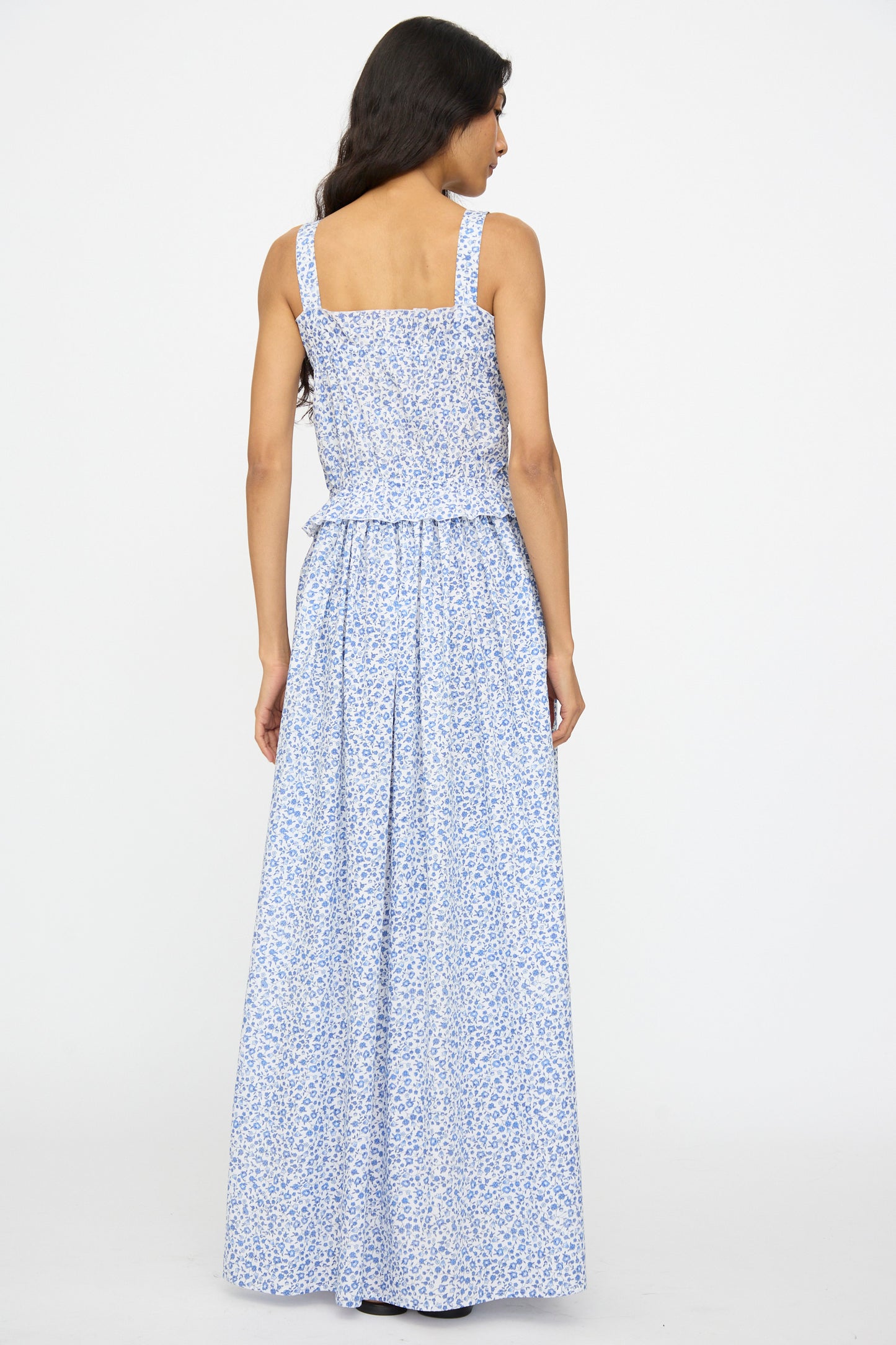 Woman standing with her back to the camera, wearing the Ombretta Dress in Marina Grande by Loretta Caponi, a light blue floral printed cotton maxi dress.