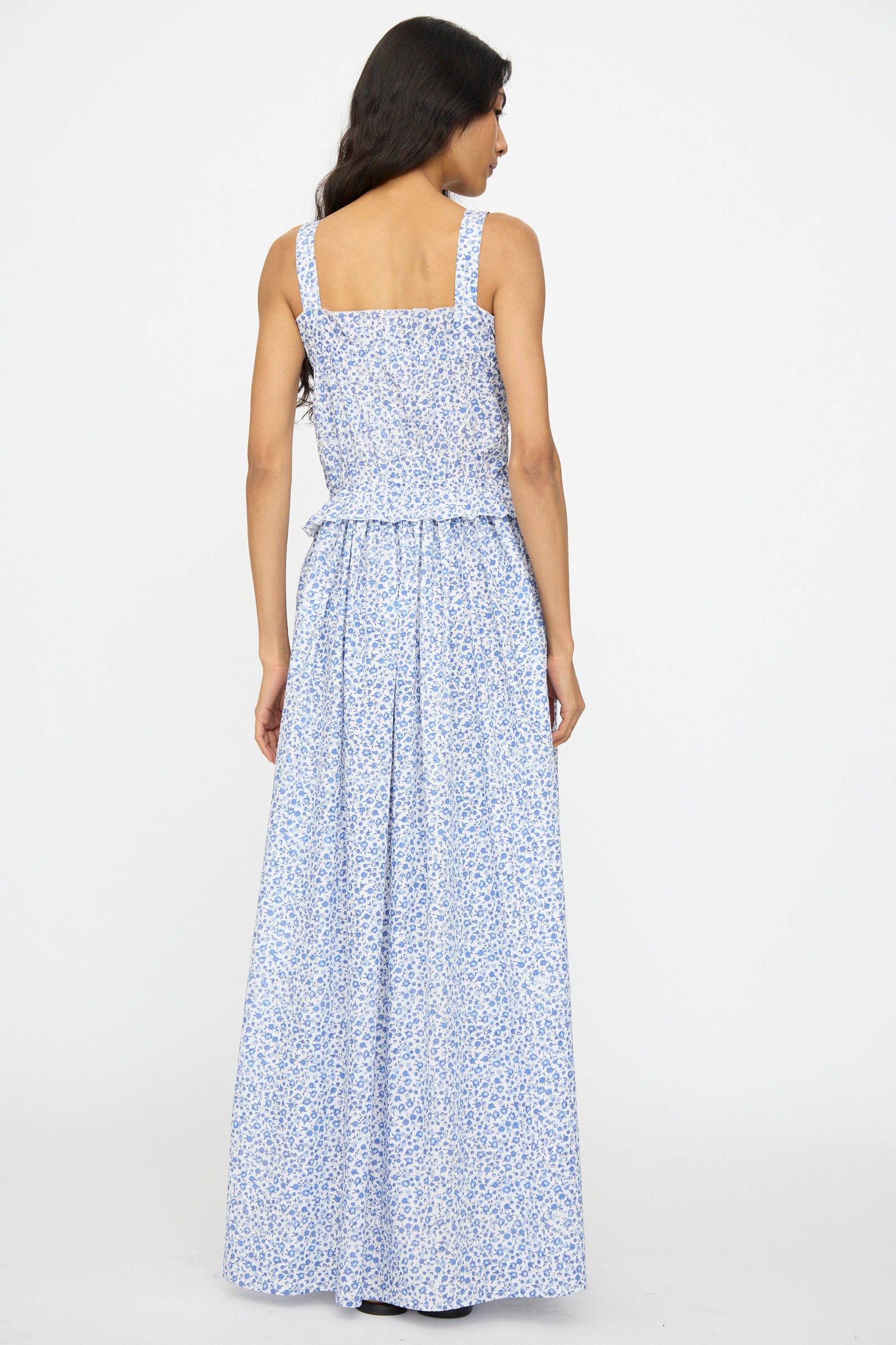 Woman standing with her back to the camera, wearing the Ombretta Dress in Marina Grande by Loretta Caponi, a light blue floral printed cotton maxi dress.