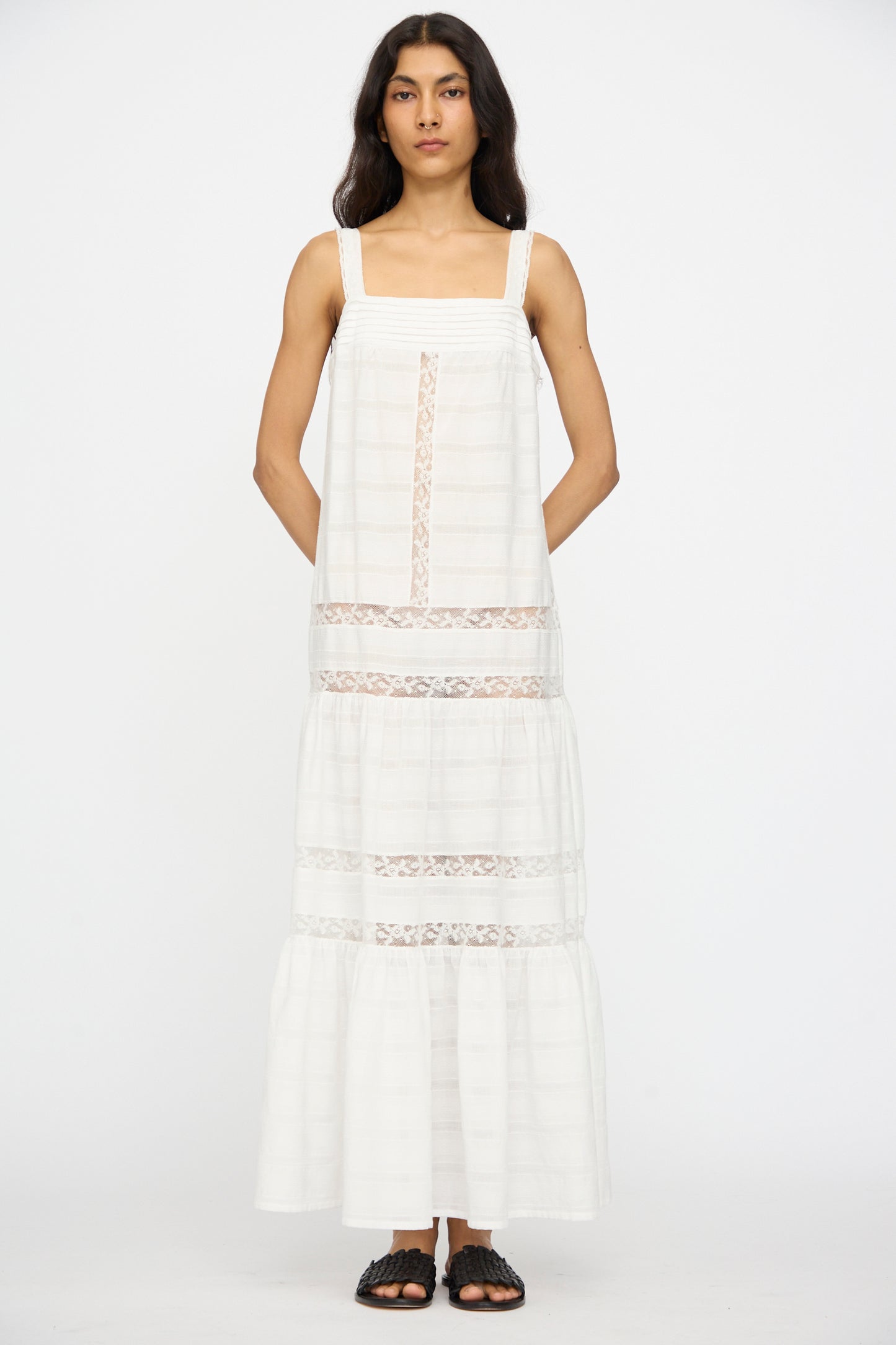 A person stands facing forward, wearing the Loretta Caponi Populonia Dress in Off White with black sandals, against a plain white background.