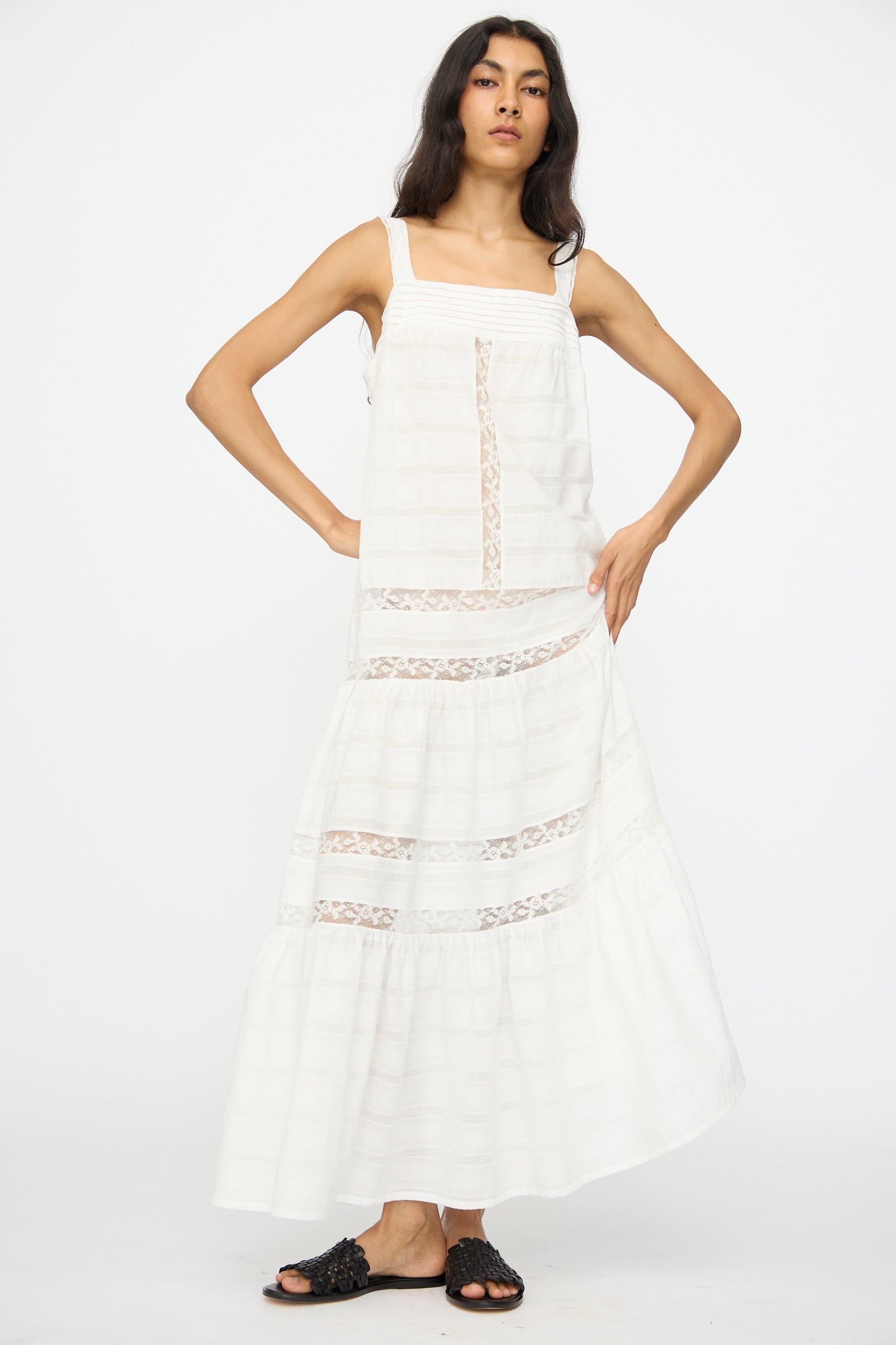 A woman stands against a white background wearing the Loretta Caponi Populonia Dress in Off White and black slide sandals.