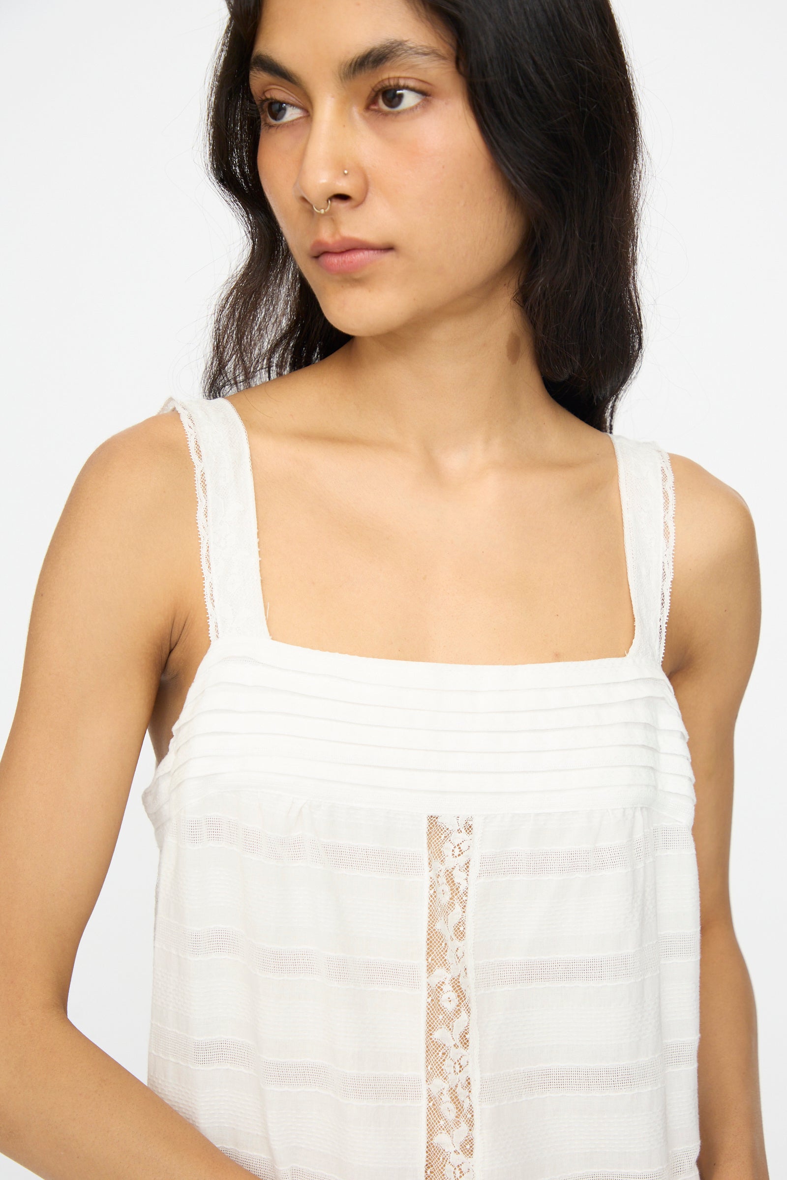 A person with long dark hair wears the Loretta Caponi Populonia Dress in Off White, featuring delicate lace details, and looks slightly to the side against a plain background.