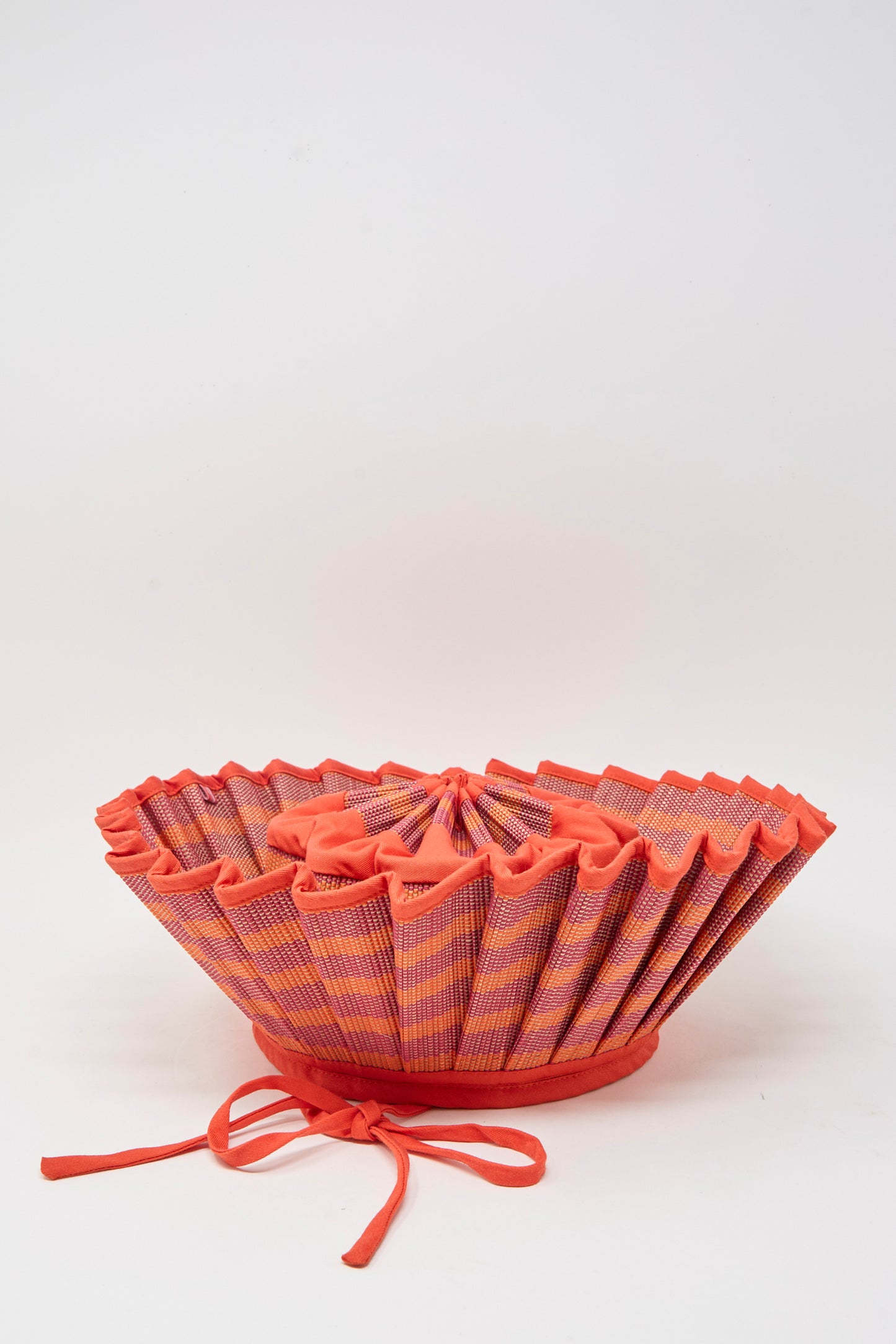 The Island Capri Hat in Bossa Nova by Lorna Murray is a pleated, striped sun hat crafted from natural grass fibers with red trim and ribbons, UPF 50+ protection, shown upside down on a plain white background.