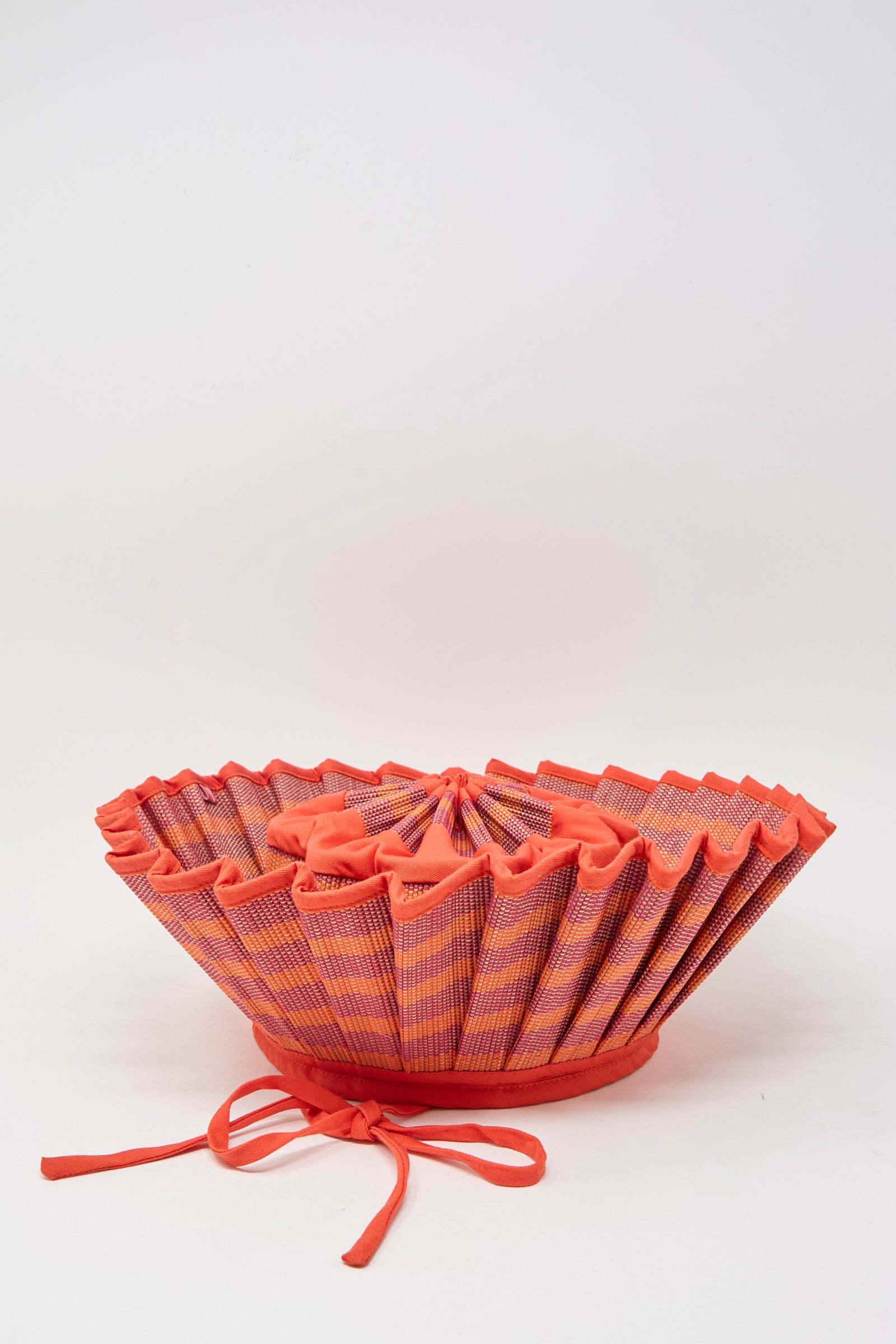 The Island Capri Hat in Bossa Nova by Lorna Murray is a pleated, striped sun hat crafted from natural grass fibers with red trim and ribbons, UPF 50+ protection, shown upside down on a plain white background.