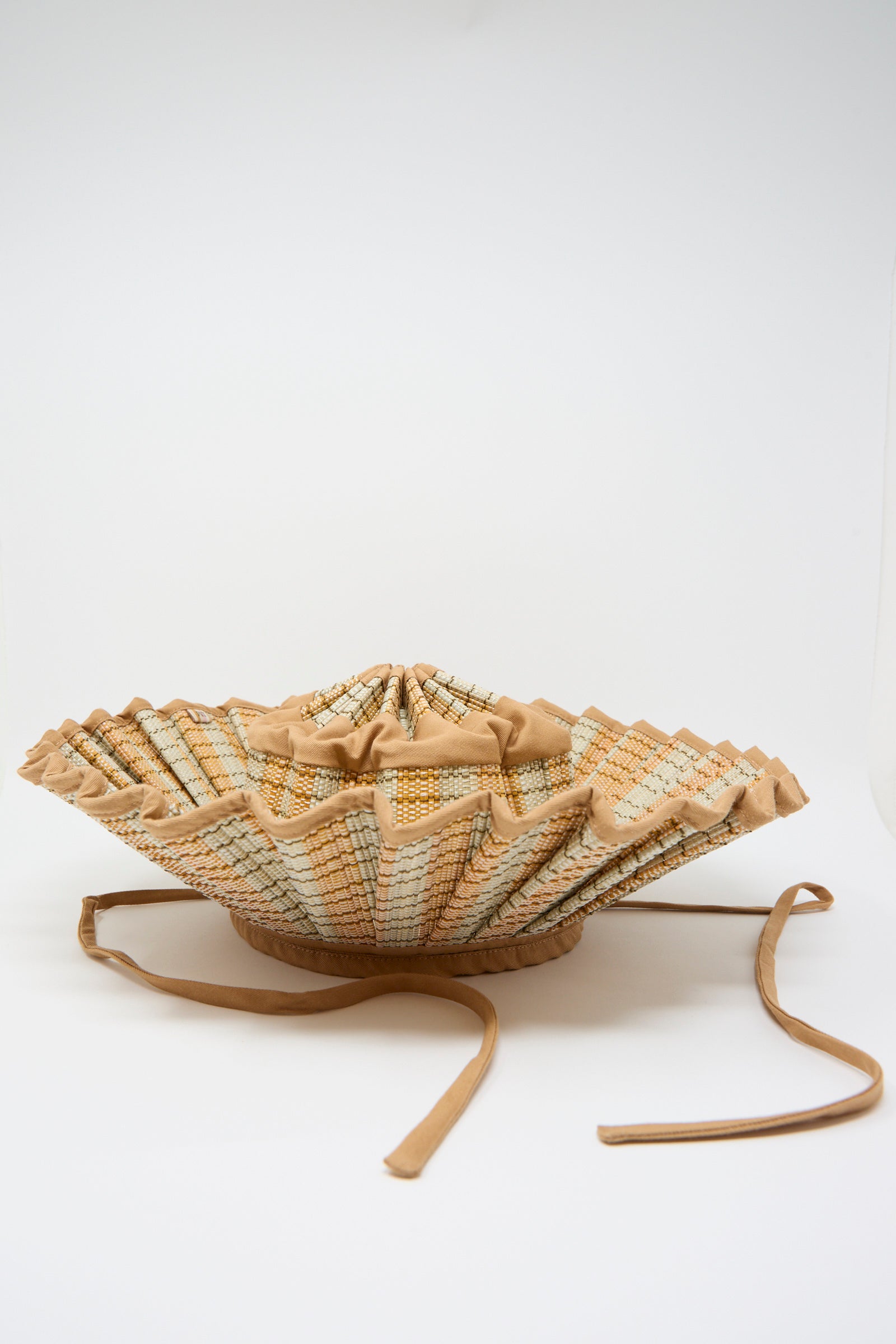 The Island Capri Maxi Hat in Petra by Lorna Murray is a pleated sun hat made of natural grass fibers with a wide, structured brim in beige and light patterns, two long ties, UPF 50+ protection, shown on a white background.