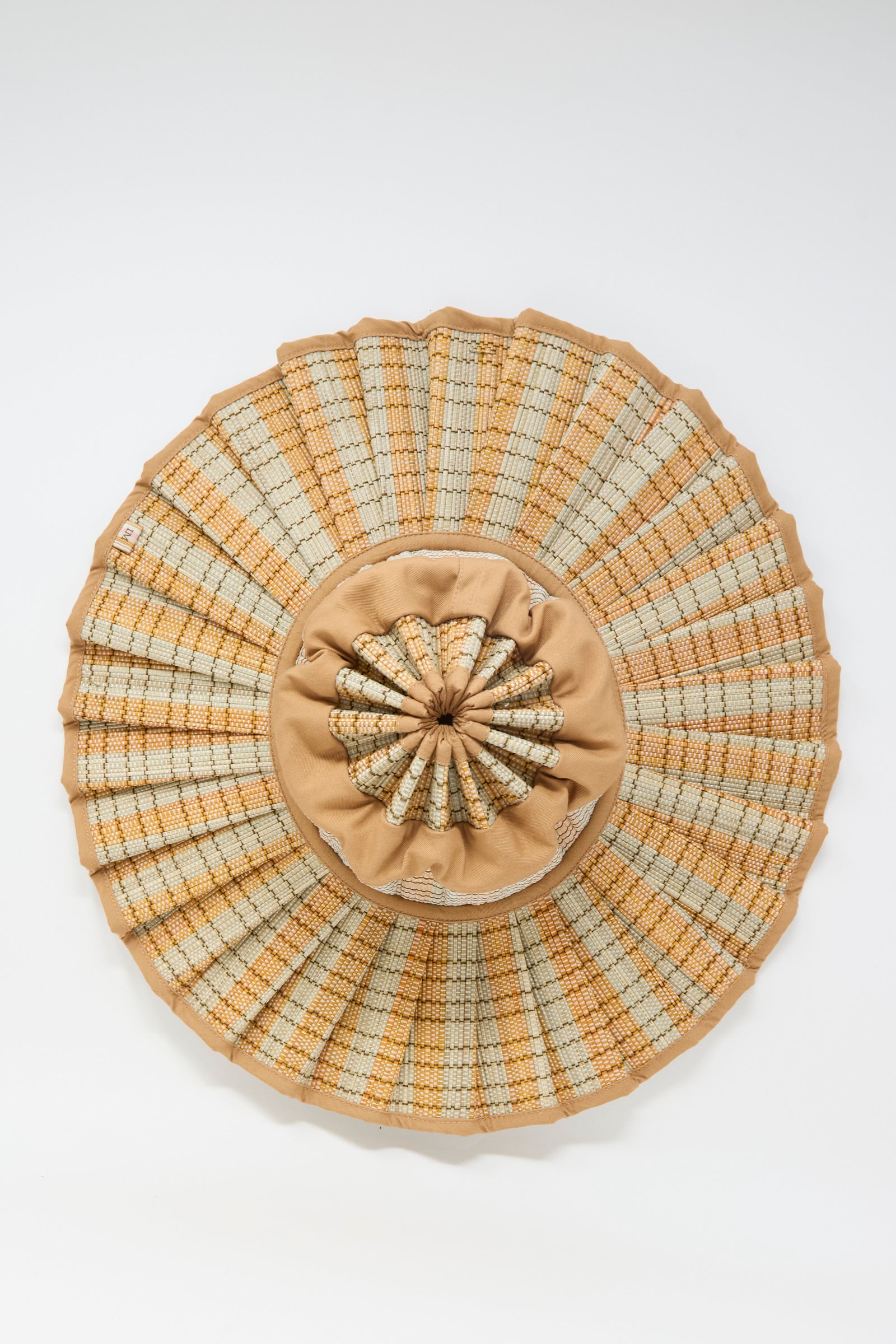 The Island Capri Maxi Hat in Petra by Lorna Murray is a round, woven sun hat in beige and tan, crafted from natural grass fibers with a pleated brim and gathered fabric center, offering UPF 50+ protection. Shown on a plain white background.