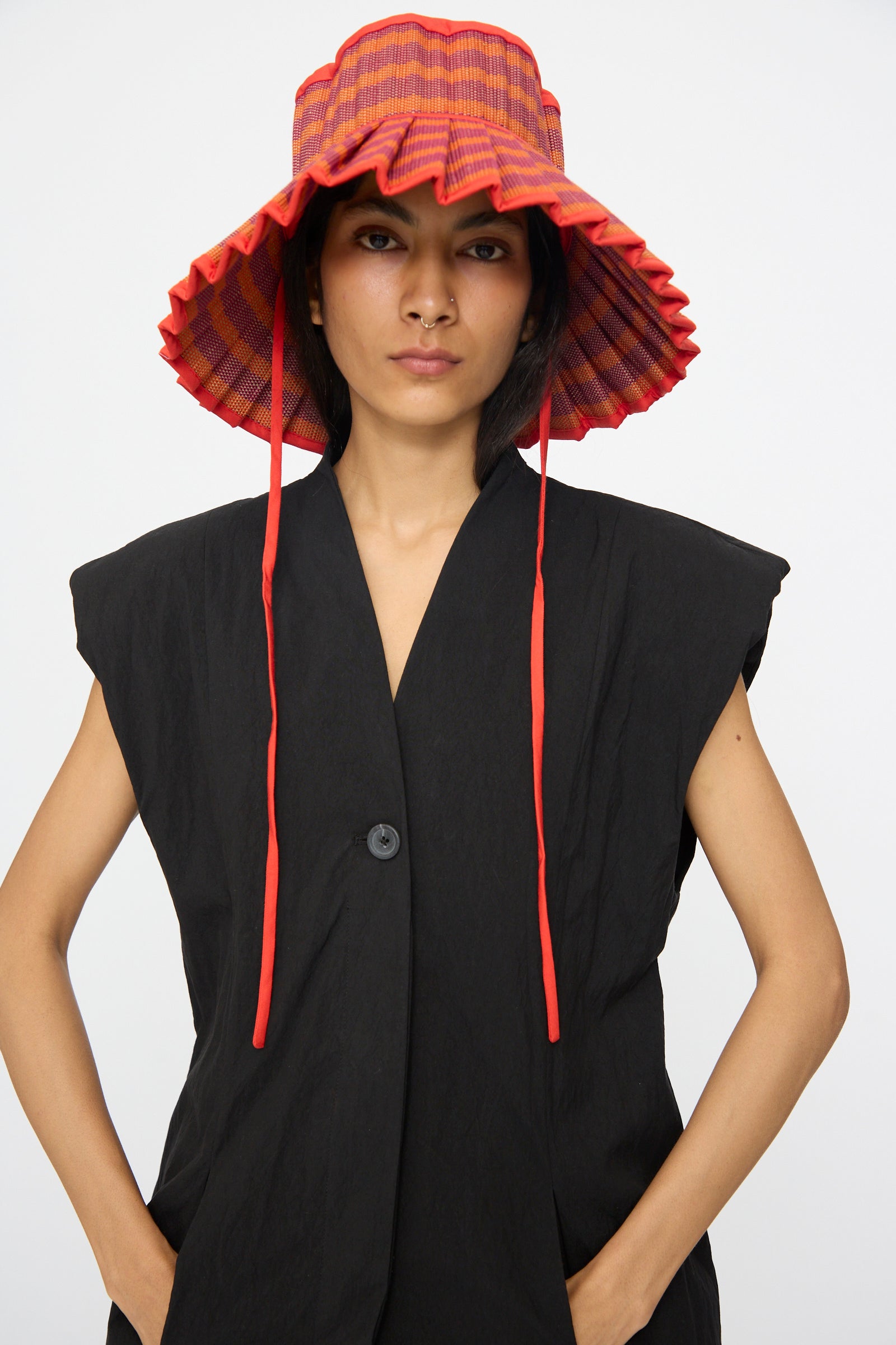 A person wears the Lorna Murray Island Capri Hat in Bossa Nova—a wide-brimmed, red-striped sun hat with ruffled edges and chin straps—standing against a white background.