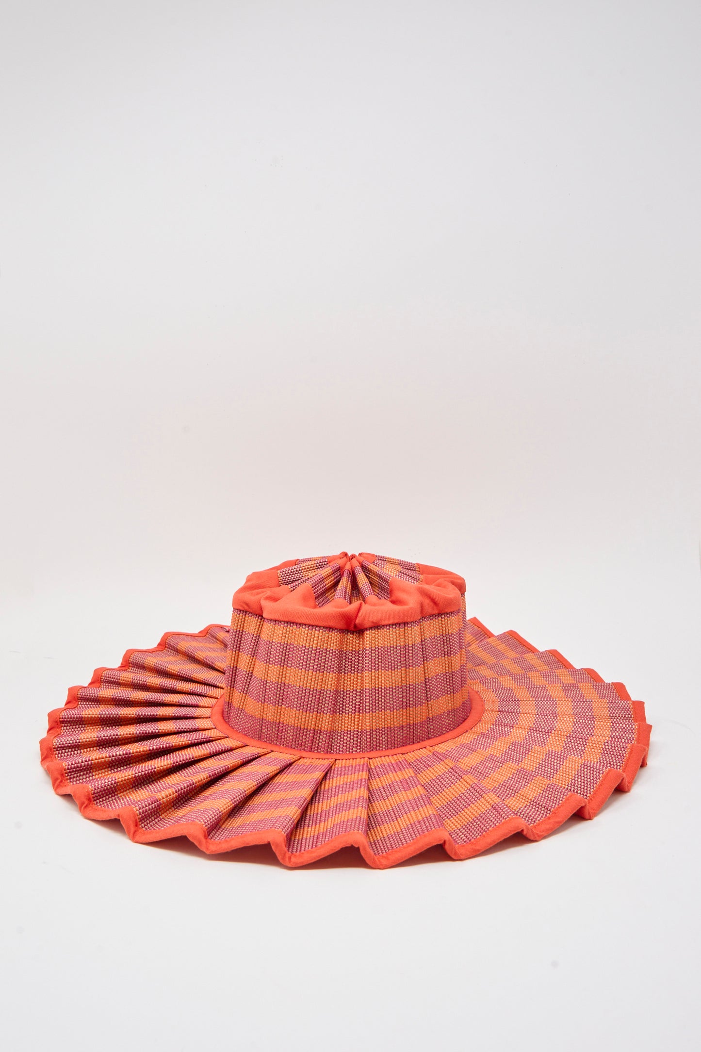 The Lorna Murray Island Capri Hat in Bossa Nova features pleated edges, crafted from natural grass fibers with orange, pink, and purple woven patterns. Offers UPF 50+ protection and is displayed on a plain white background.