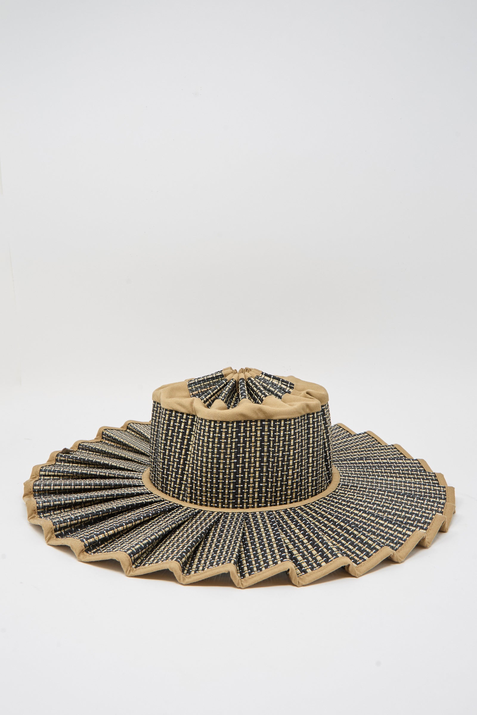 The Lorna Murray Island Capri Maxi Hat in Nara features a pleated black and tan design, woven from natural grass fibers, offers UPF 50+ sun protection, and is displayed against a plain white background.