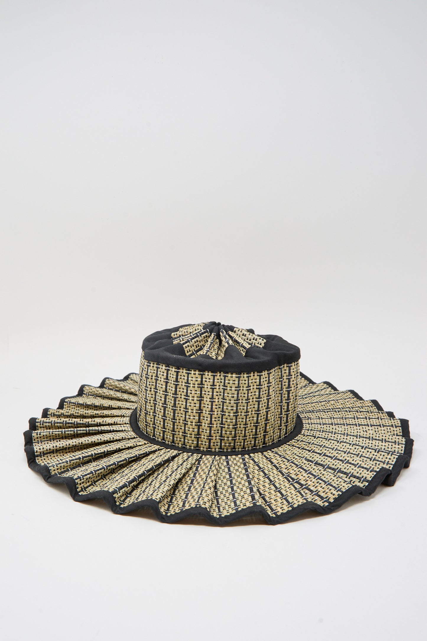 The Island Capri Maxi Hat in Lovers Point by Lorna Murray is a woven sun hat made from natural grass fibers with a pleated wide brim and black-beige pattern, offering UPF 50+ protection. Shown on a plain white background.