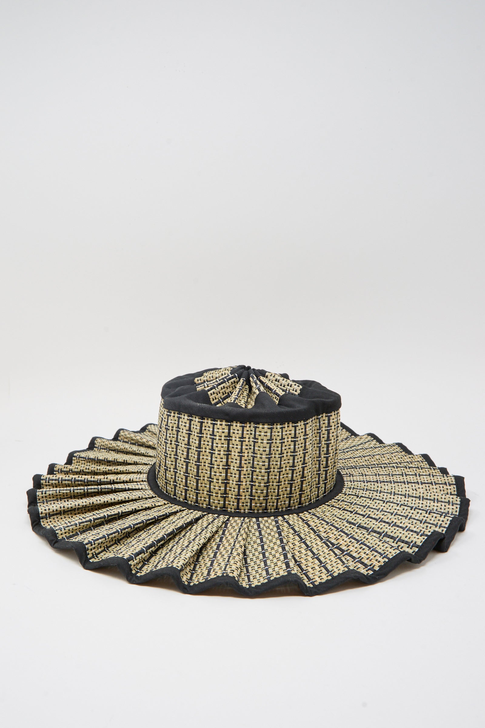 The Island Capri Maxi Hat in Lovers Point by Lorna Murray is a woven sun hat made from natural grass fibers with a pleated wide brim and black-beige pattern, offering UPF 50+ protection. Shown on a plain white background.