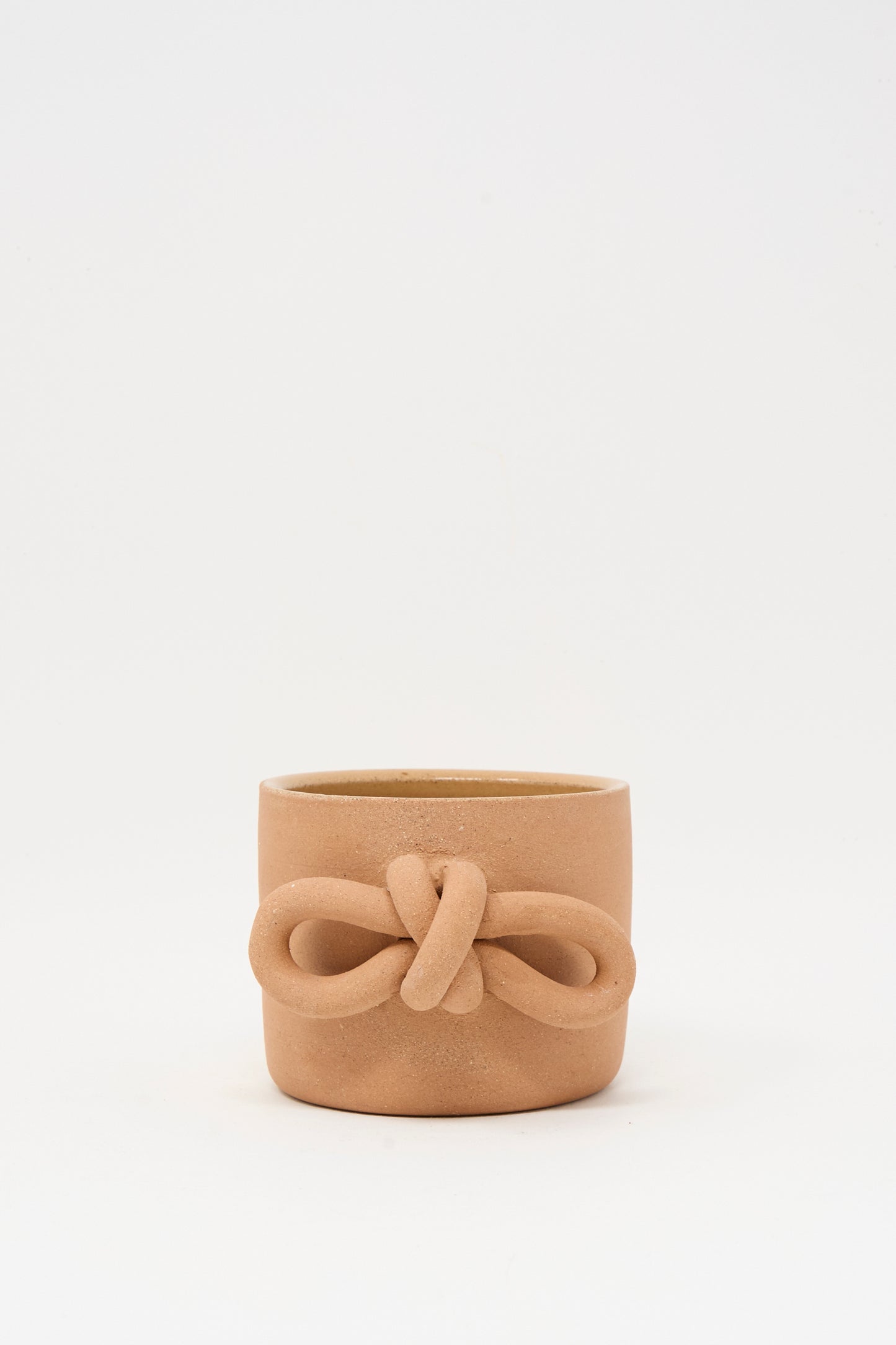 The Bow Knot Mug in Adobe by Lost Quarry is a small, unglazed terracotta mug with a decorative knot design on the front, inspired by classic Adobe Knot Mugs and shown against a plain white background.