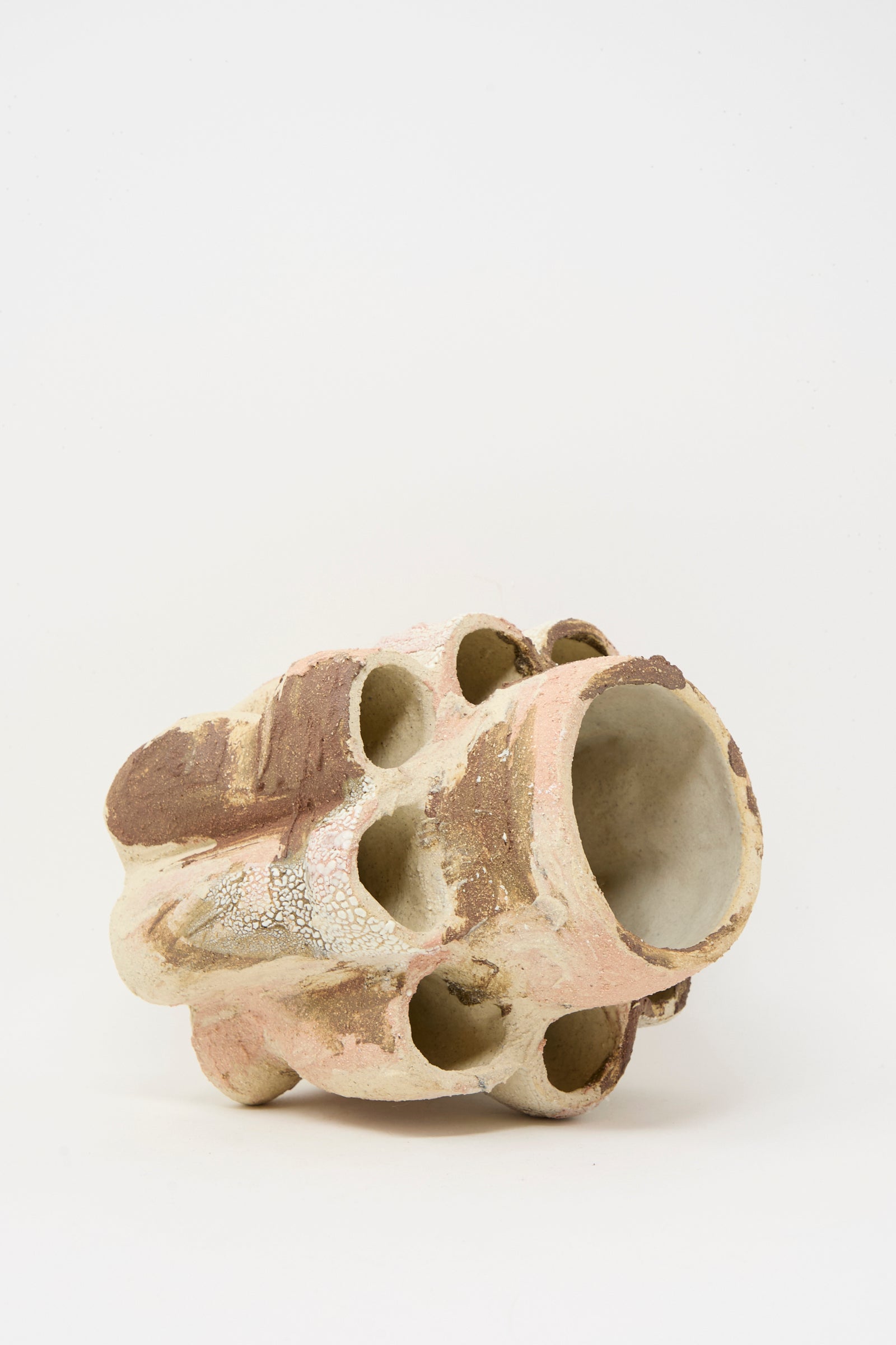 The Hand Built Clay Tulipiere Vessel from Lost Quarry features an organic, irregular shape with rounded holes and a textured surface in beige, brown, and pink tones.