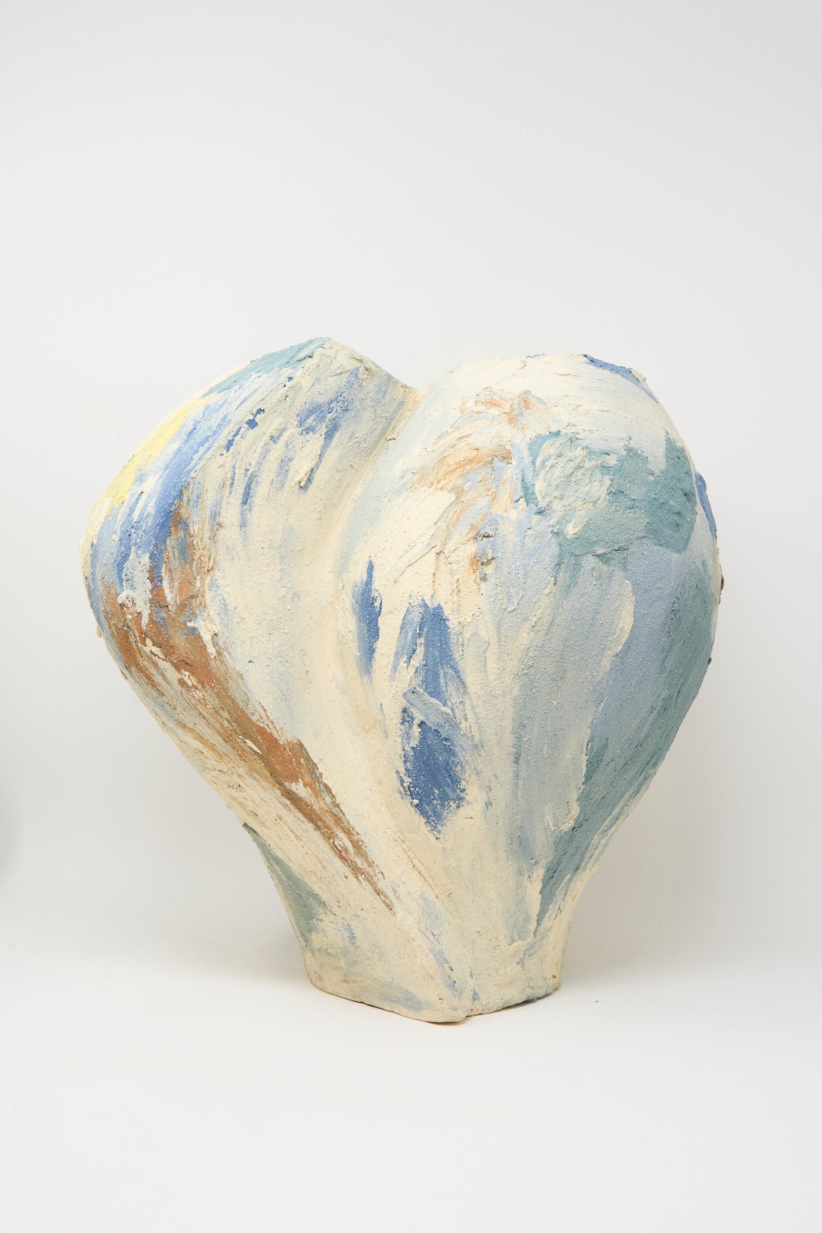 The Hand Built Cloudy Day Vessel by Lost Quarry is a handmade, heart-shaped ceramic piece with a rough texture, crafted from sculptural clay and painted in pastel blue, beige, and brown against a plain white background.