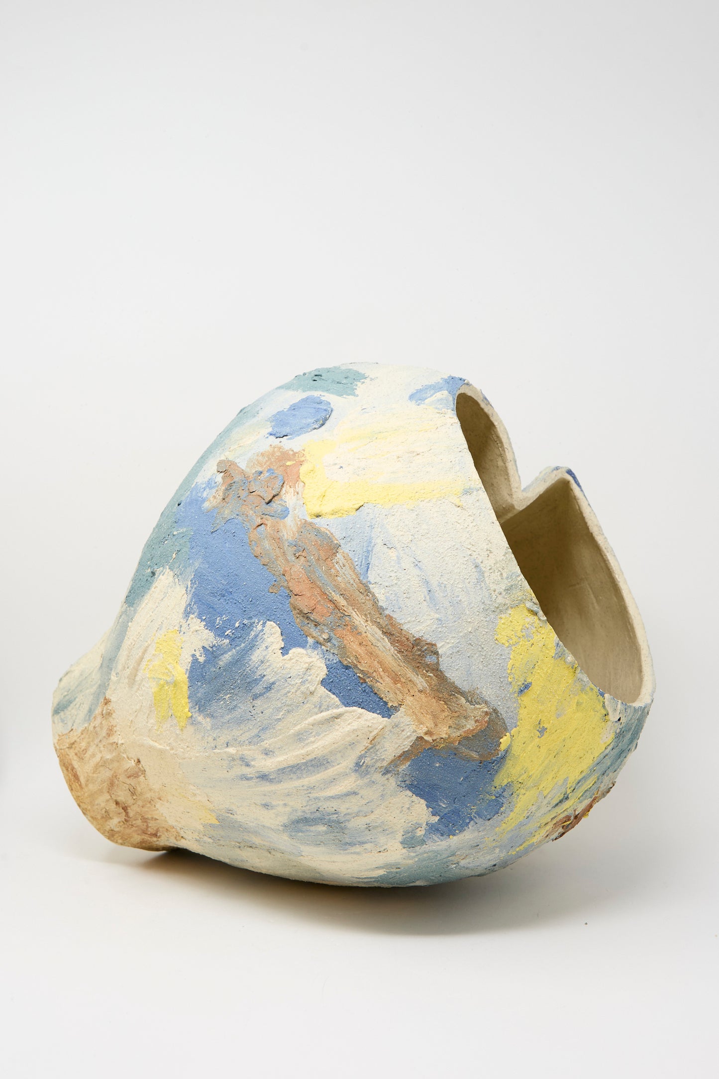 The Hand Built Cloudy Day Vessel by Lost Quarry is a uniquely shaped ceramic piece featuring a wide opening and abstract blue, yellow, and beige brushstrokes on a neutral base.
