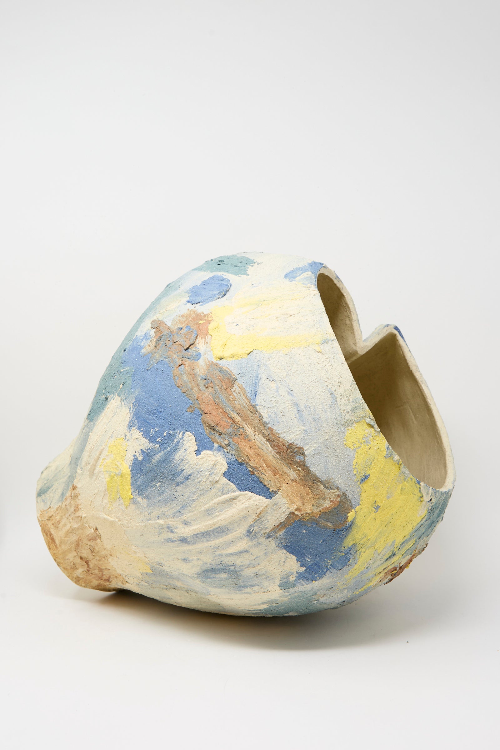 The Hand Built Cloudy Day Vessel by Lost Quarry is a uniquely shaped ceramic piece featuring a wide opening and abstract blue, yellow, and beige brushstrokes on a neutral base.