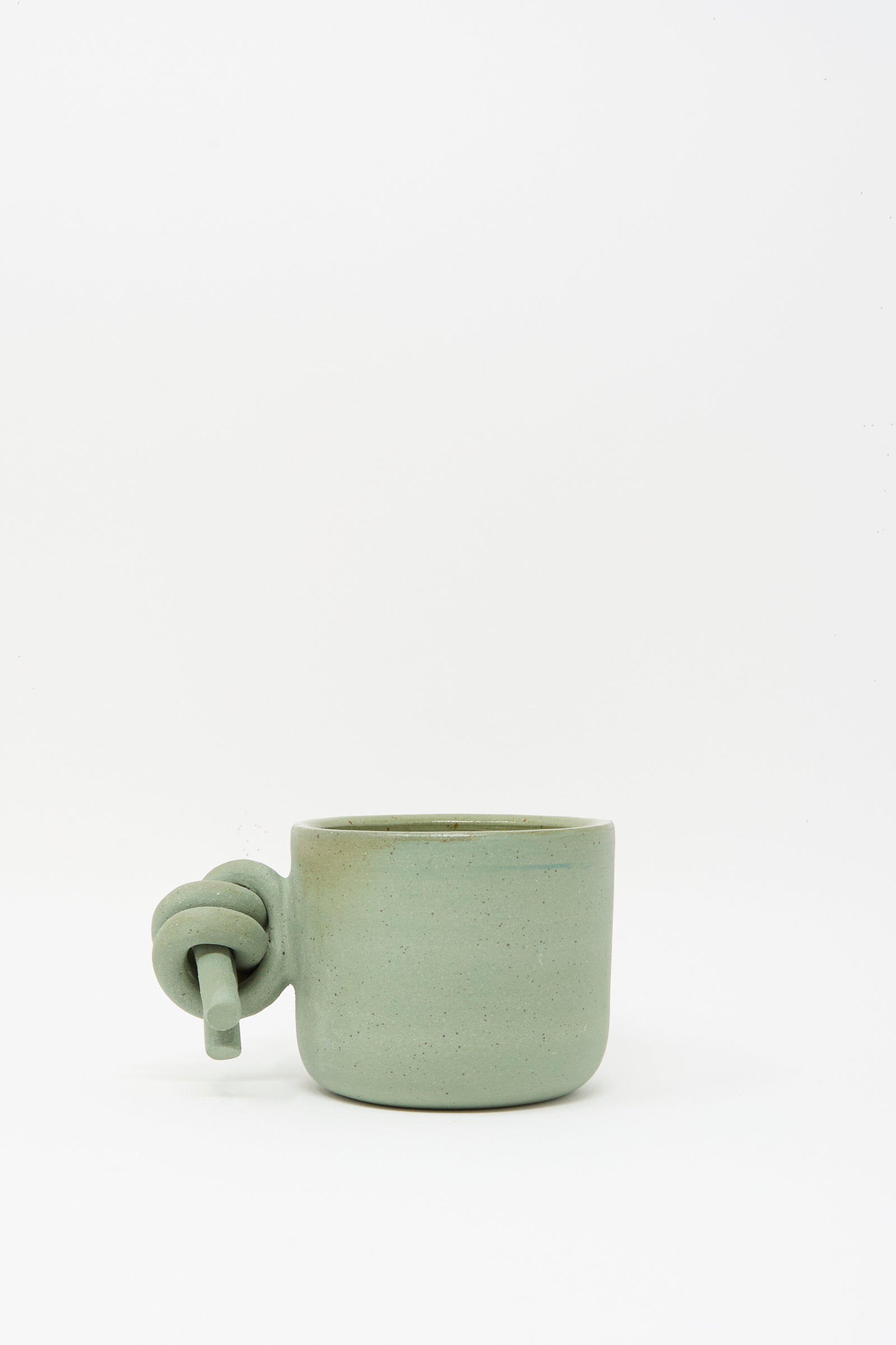 The Hand Built Knot Mug in Sage I by Lost Quarry is a light green handmade ceramic mug featuring a unique oversized handle, displayed against a plain white background.