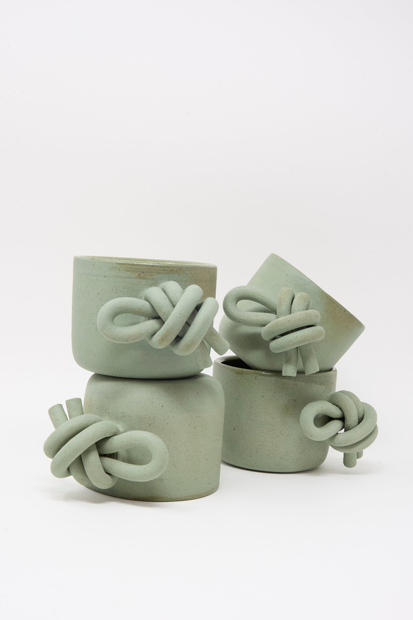 Four Hand Built Knot Mugs in Sage I by Lost Quarry, featuring twisted oversized handles, are stacked against a plain white background.
