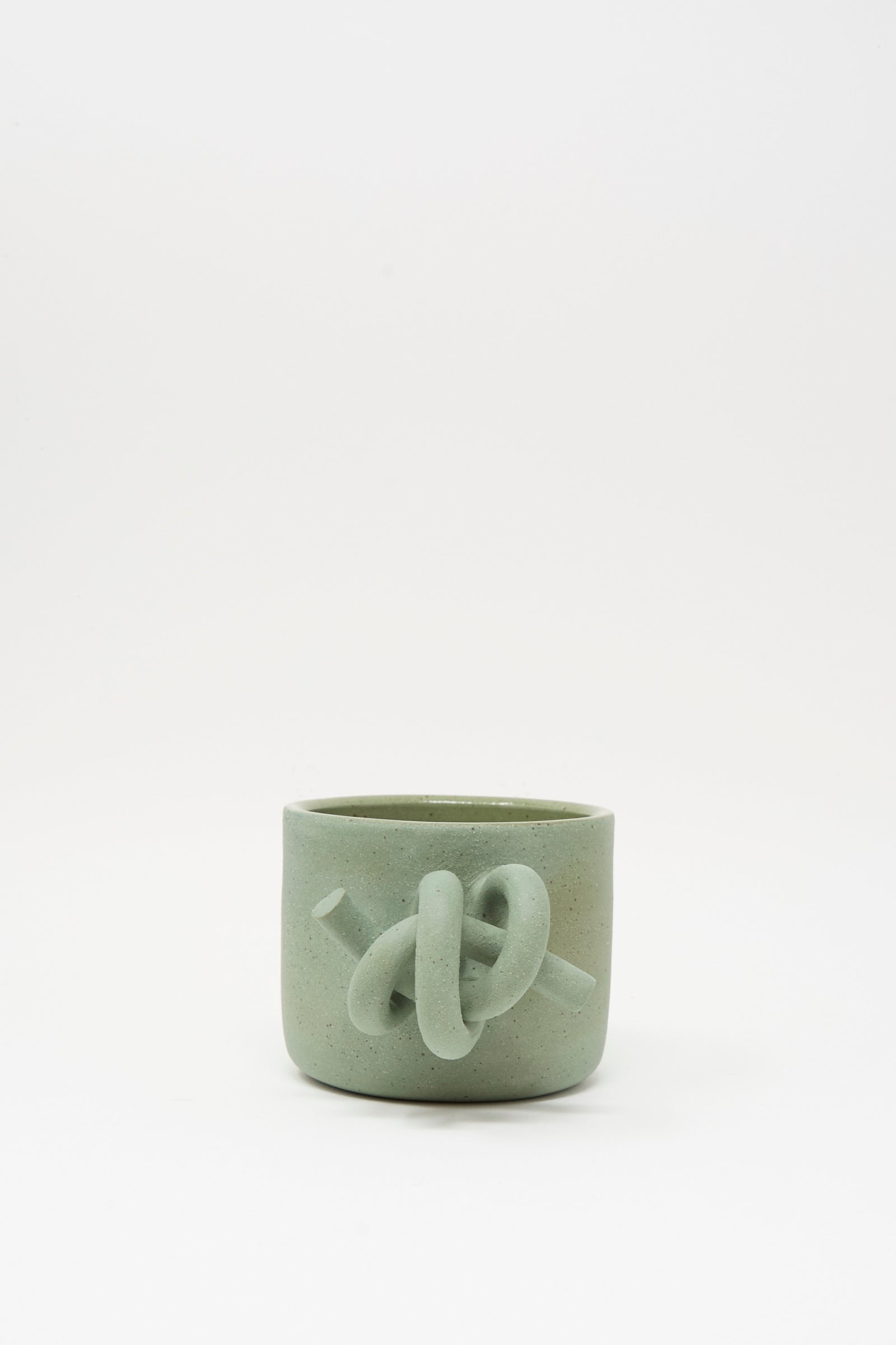 The Hand Built Knot Mug in Sage II by Lost Quarry is a light green ceramic mug with a sculpted knot design and smooth sage glaze, shown against a plain white background.