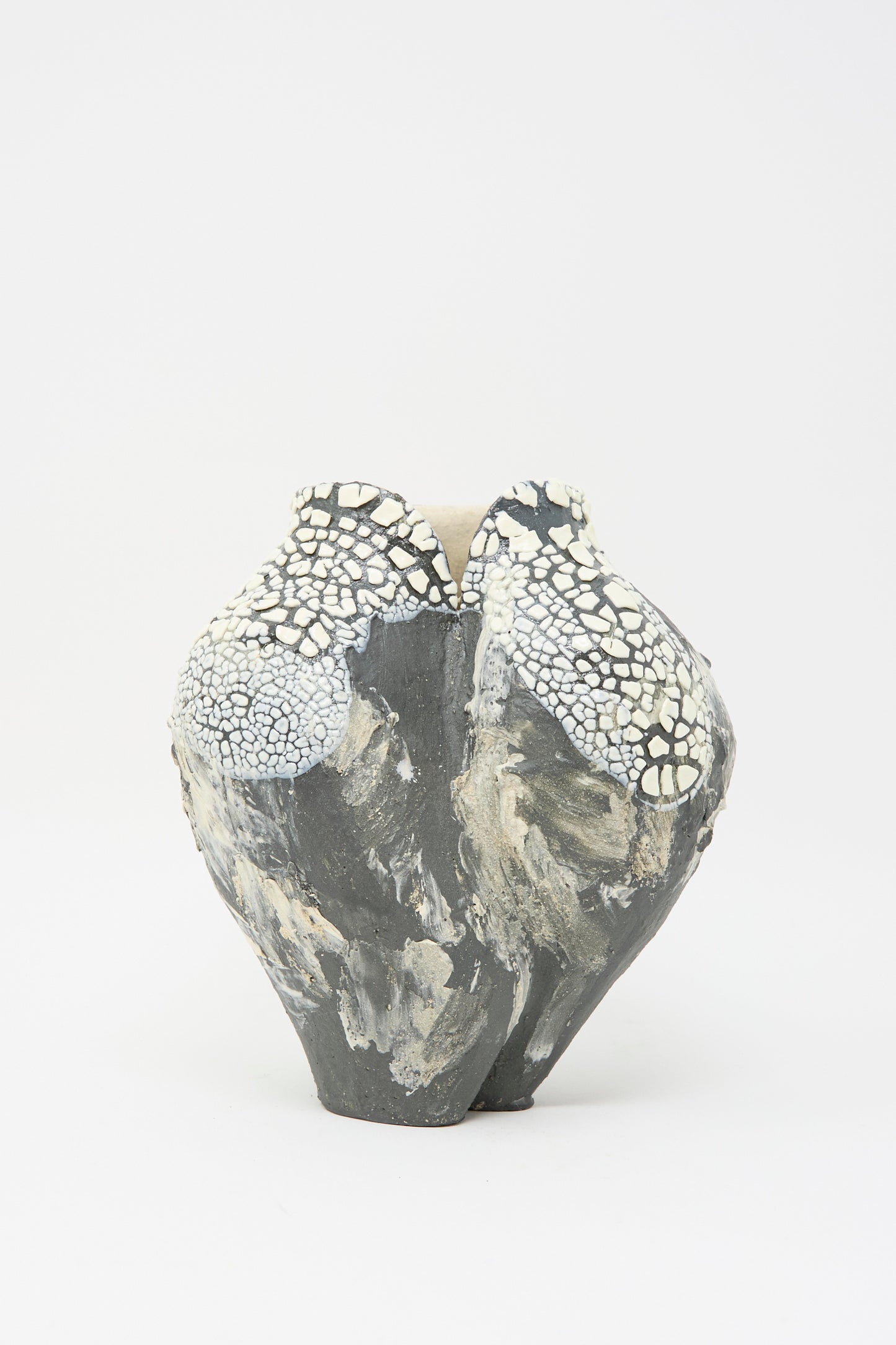 The Lost Quarry "Hand Built Textured Vessel in Black and White" showcases a sculptural ceramic form with a rough, irregular surface. Its rounded shape features mottled dark grey and white crackled patterns for a textured appearance.