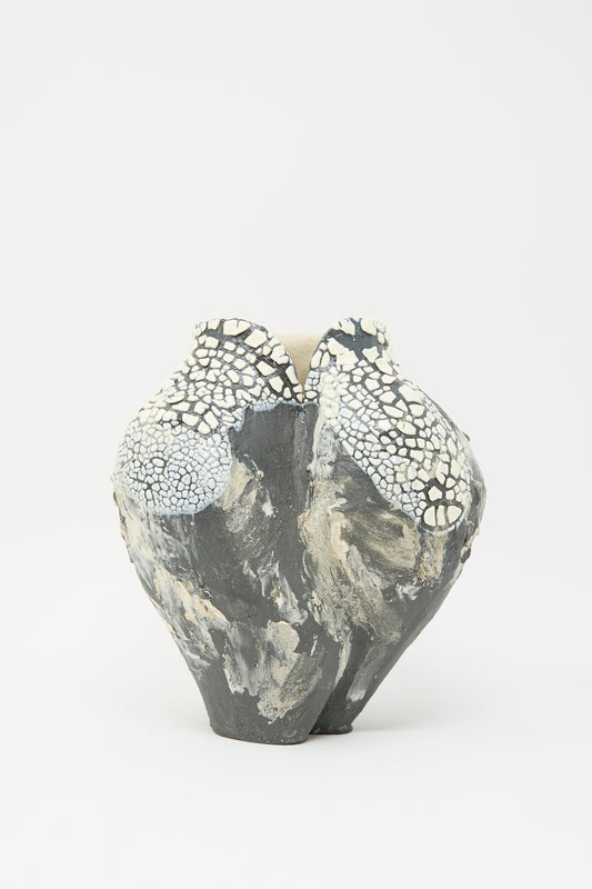 The Lost Quarry "Hand Built Textured Vessel in Black and White" showcases a sculptural ceramic form with a rough, irregular surface. Its rounded shape features mottled dark grey and white crackled patterns for a textured appearance.