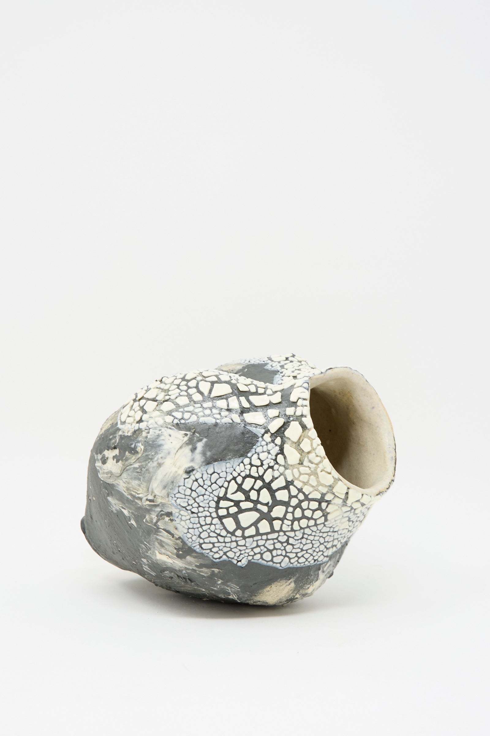 The Hand Built Textured Vessel in Black and White by Lost Quarry is seen on its side, showcasing a sculptural clay design with a rounded, organic shape, featuring a mix of black and white crackle patterns on its plain background, enhanced by its textured glaze.