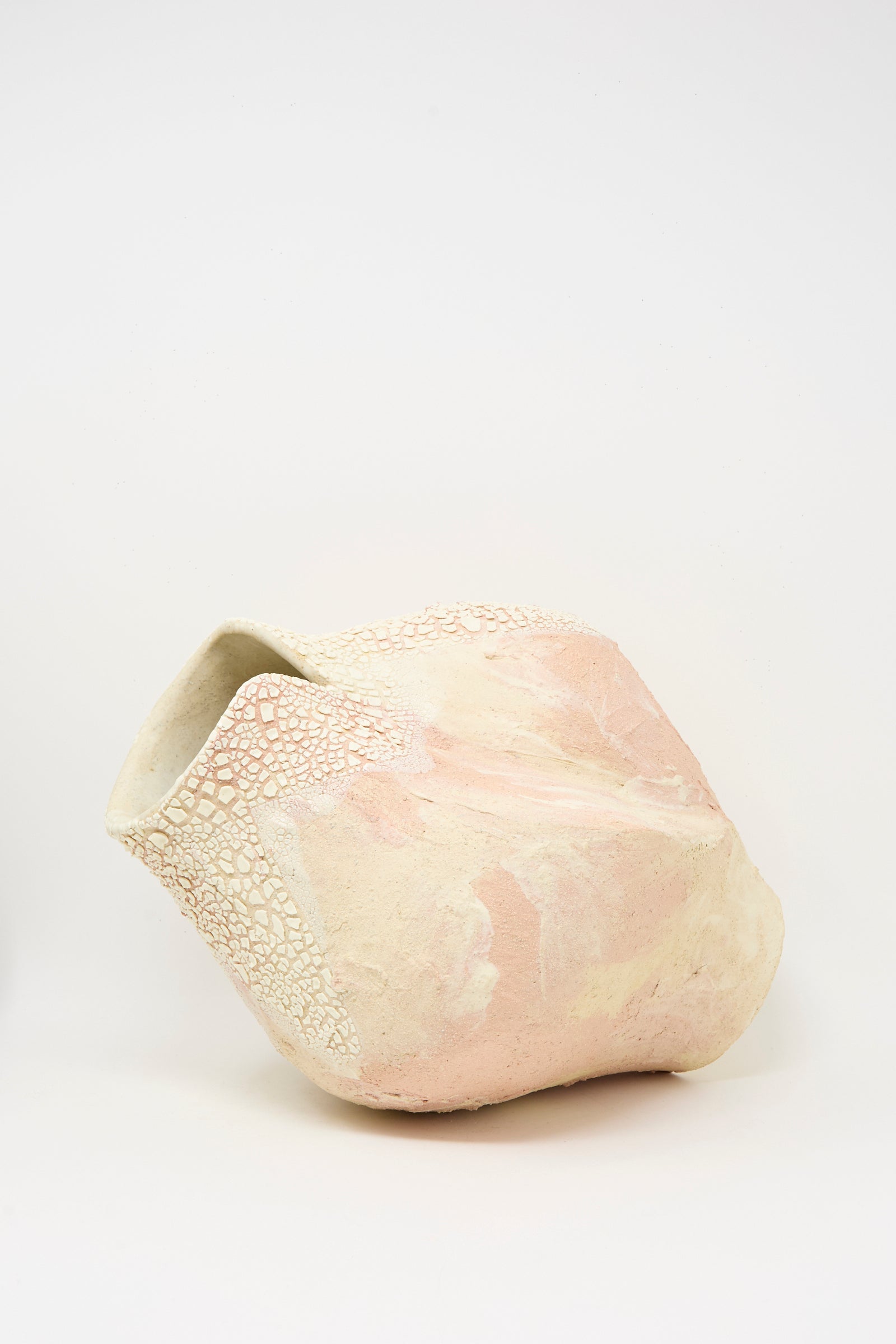 The Lost Quarry Hand Built Textured Vessel in Pale Pink features a rough, asymmetrical ceramic design in pale pink and cream, displayed against a plain white background.
