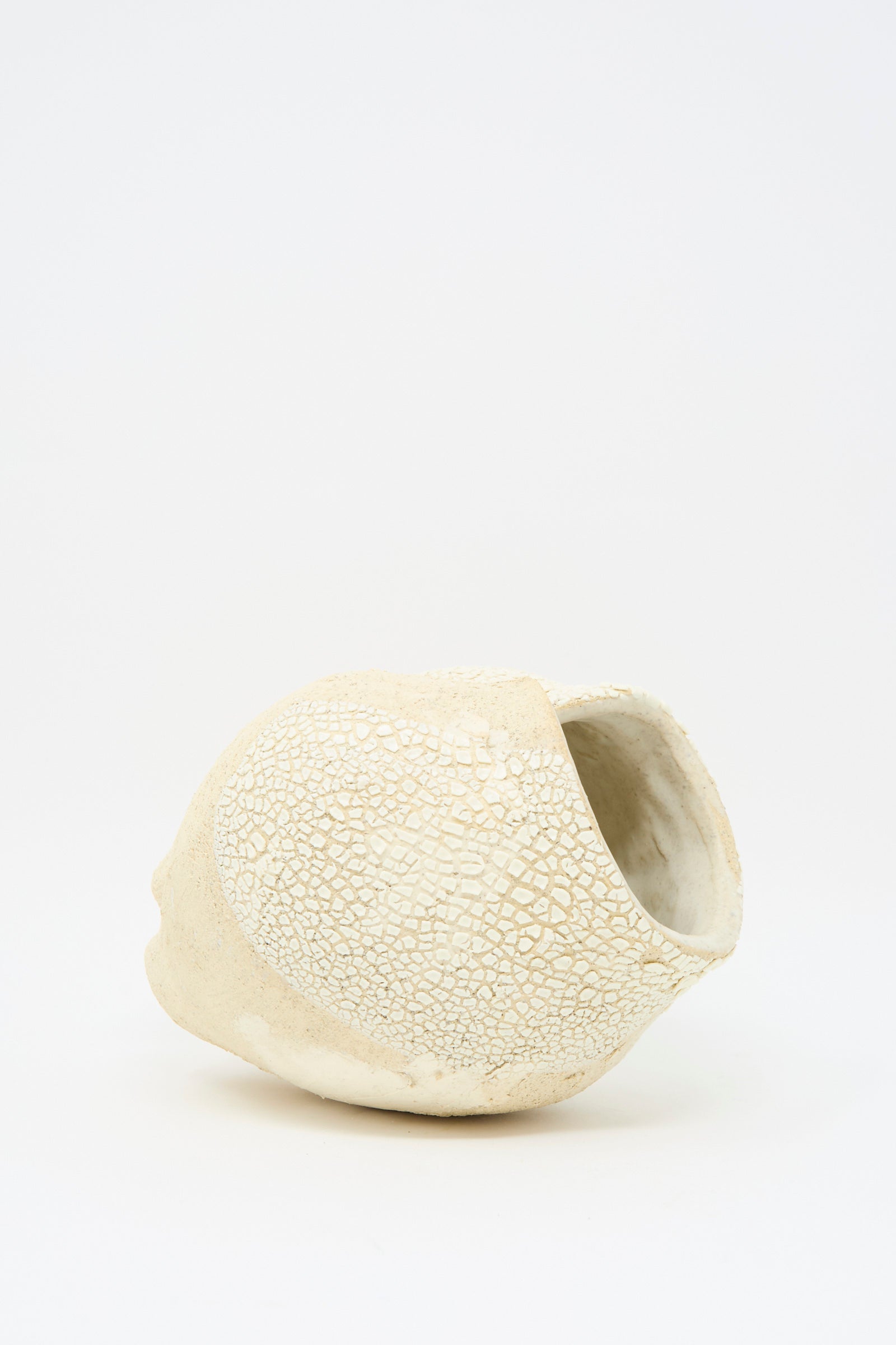 The Hand Built Textured Vessel in Neutral and White by Lost Quarry features an irregular beige ceramic design with a cracked surface and sculptural clay detailing, set on its side against a plain white background.