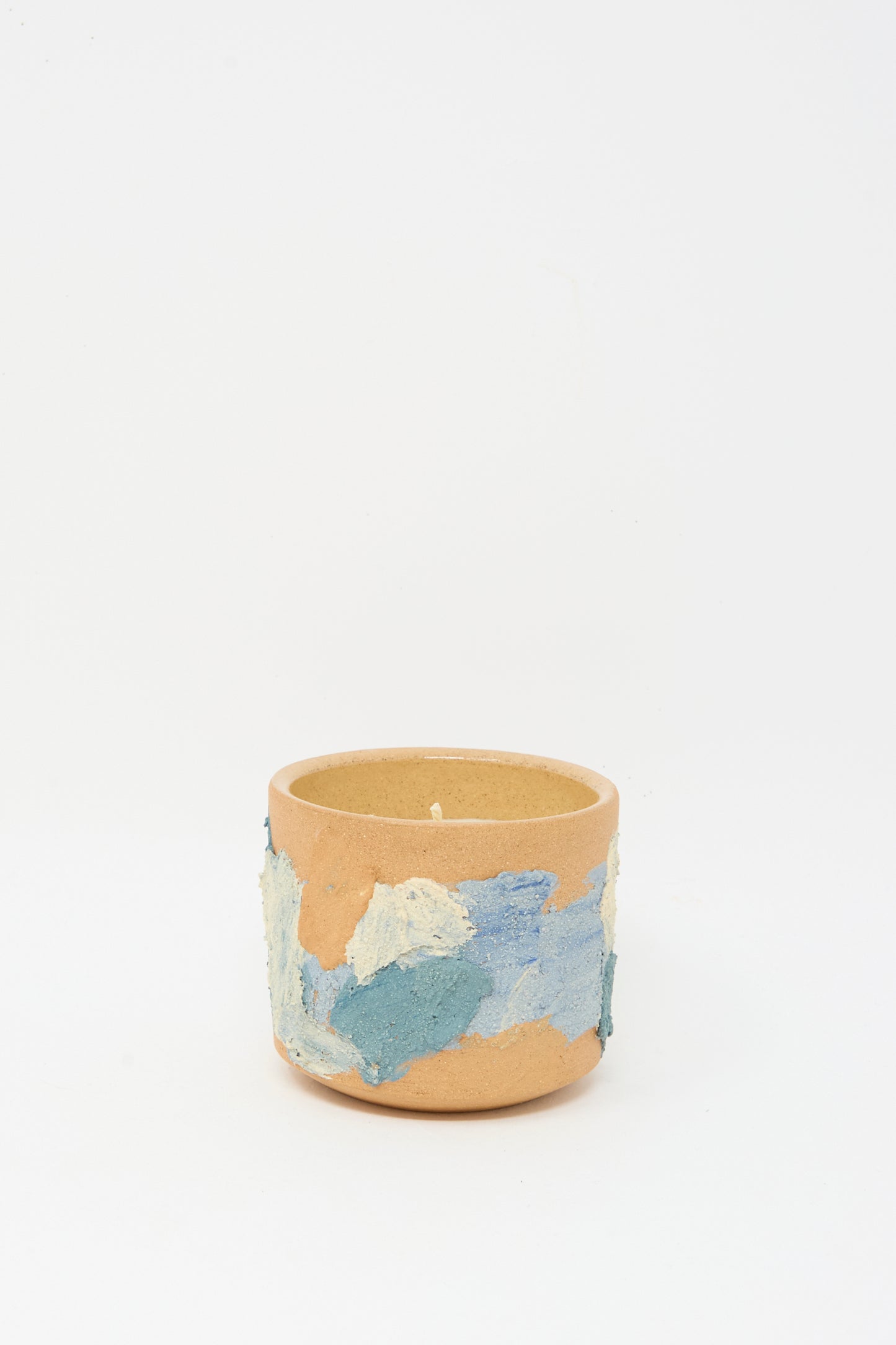 The Lost Quarry Neroli Candle in Blue Terracotta is a round, tan hand-built ceramic vessel with textured blue, white, and light brown patches—ideal for displaying a scented candle.