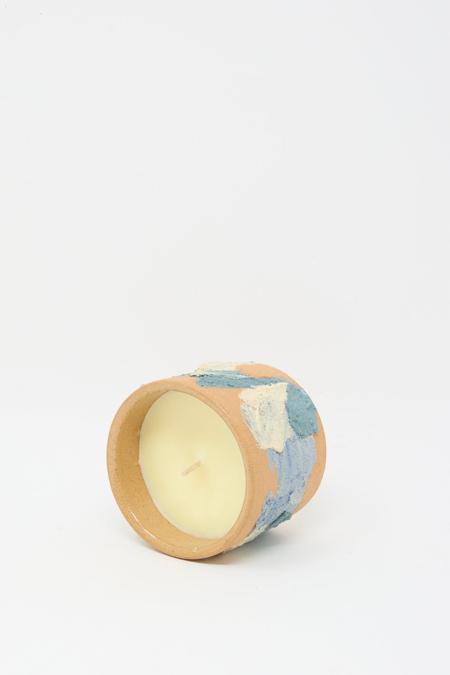 The Lost Quarry Neroli Candle in Blue Terracotta features a handmade ceramic vessel with a blue and white textured design, shown lying on its side to reveal the unused scented candle inside.