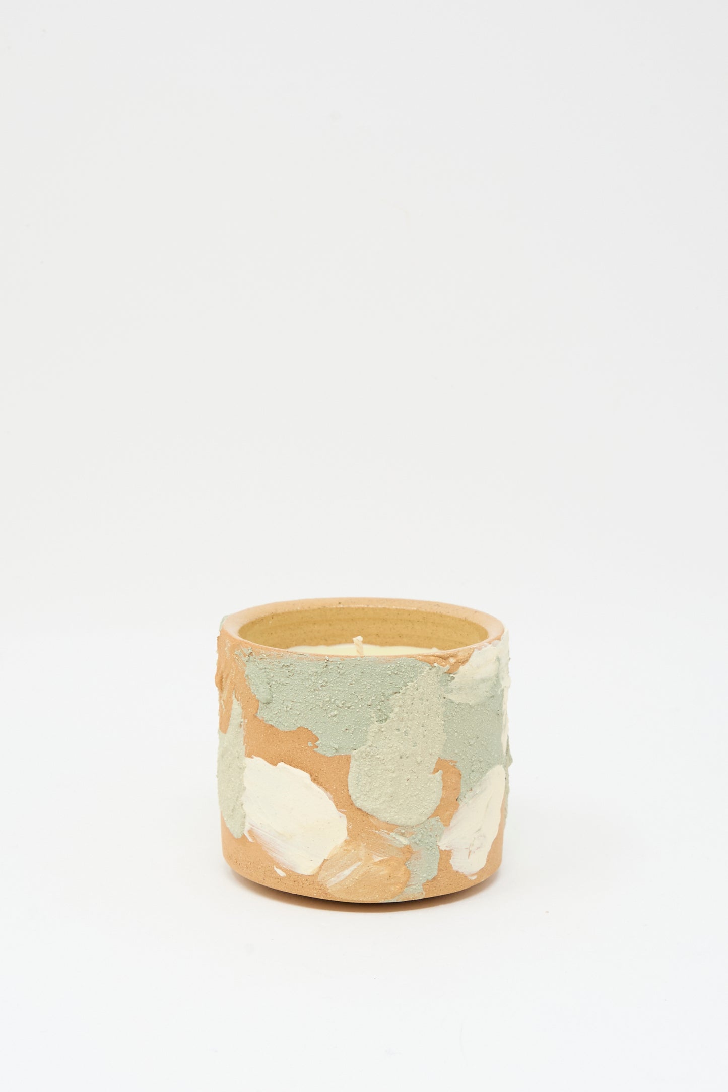 The Lost Quarry Neroli Candle in Dusty Mint Adobe Multi is a small, hand-built ceramic vessel with a textured surface and green, beige, and off-white patches, displayed against a plain white background.