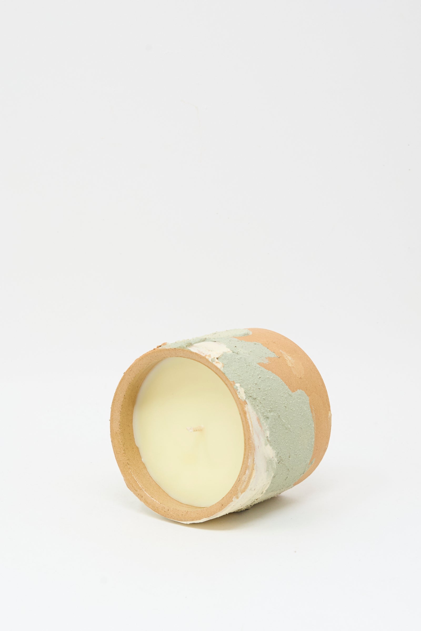 The Lost Quarry Neroli Candle in Dusty Mint Adobe Multi rests on its side against a white background, showcasing its handmade, multicolored ceramic vessel.