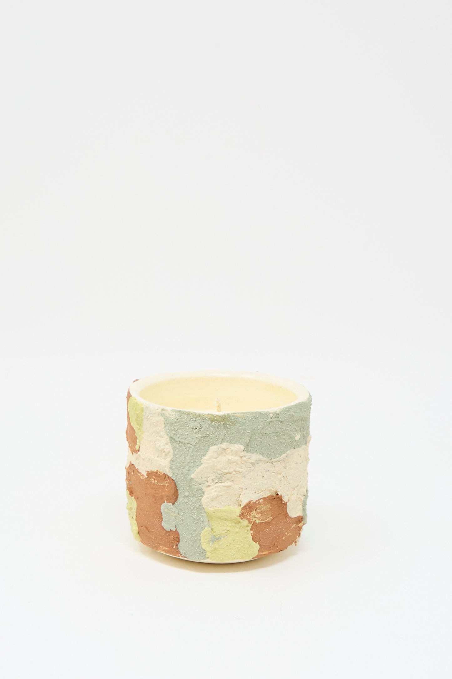 The Lost Quarry Neroli Candle in Lime Terracotta Multi features a cylindrical, hand-built ceramic vessel with a green, cream, brown, and yellow camouflage pattern, displayed against a plain white background.