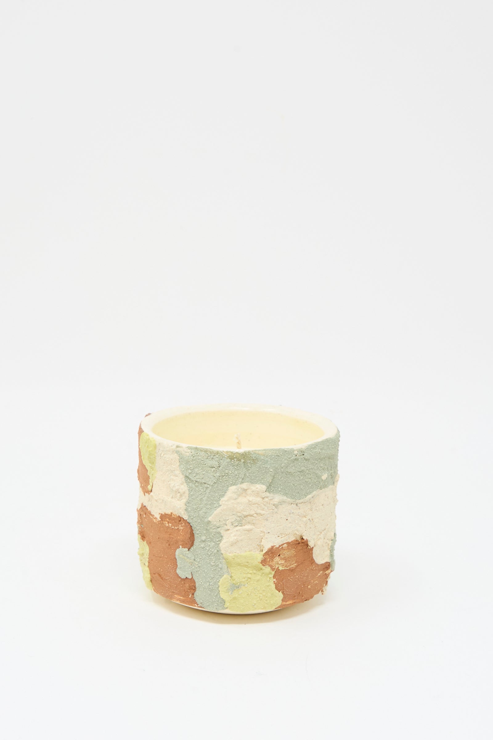 The Lost Quarry Neroli Candle in Lime Terracotta Multi features a cylindrical, hand-built ceramic vessel with a green, cream, brown, and yellow camouflage pattern, displayed against a plain white background.