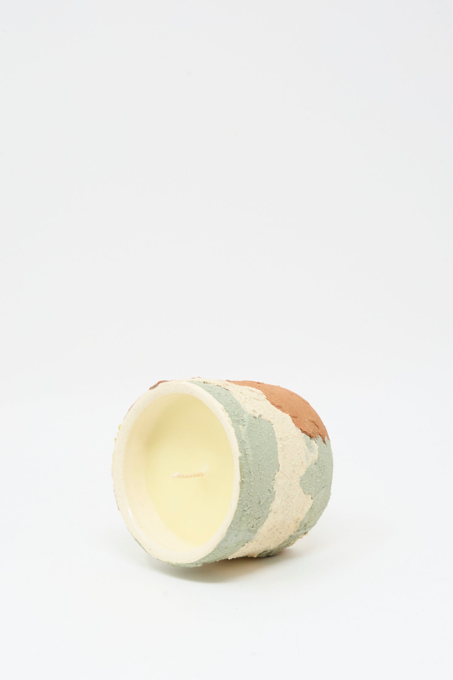The Neroli Candle in Lime Terracotta Multi by Lost Quarry is a small, round, hand-built ceramic vessel with textured beige, green, and brown patches, shown lying on its side against a plain white background.