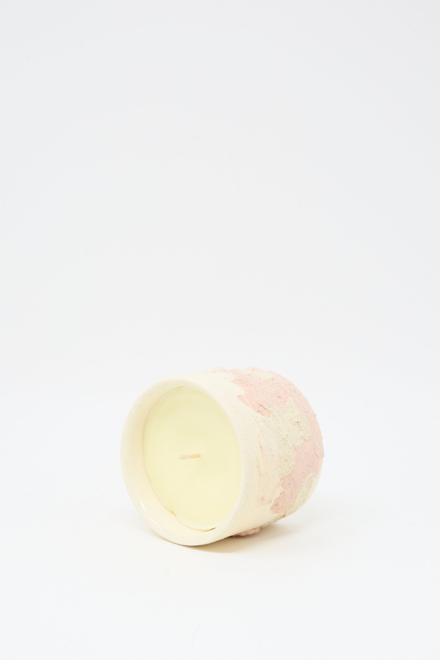 The Lost Quarry Neroli Candle in Pink Multi, a small light-colored scented candle in a hand-built ceramic vessel, rests on its side against a plain white background.