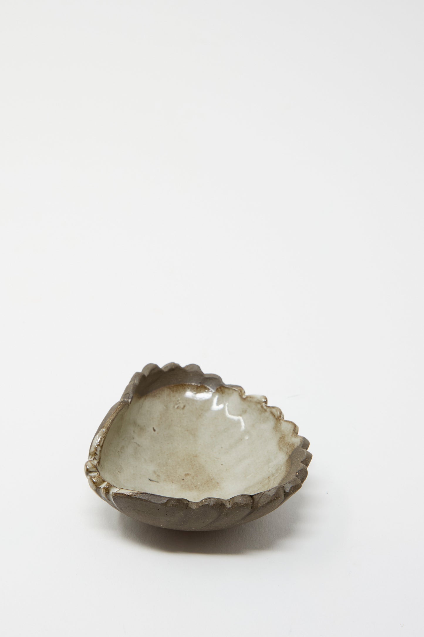 A Small Ceramic Shell Dish in Brown with a Light Glaze from Lost Quarry, featuring a handmade design with a shell-shaped, scalloped edge and a glazed surface, sits on a white background.