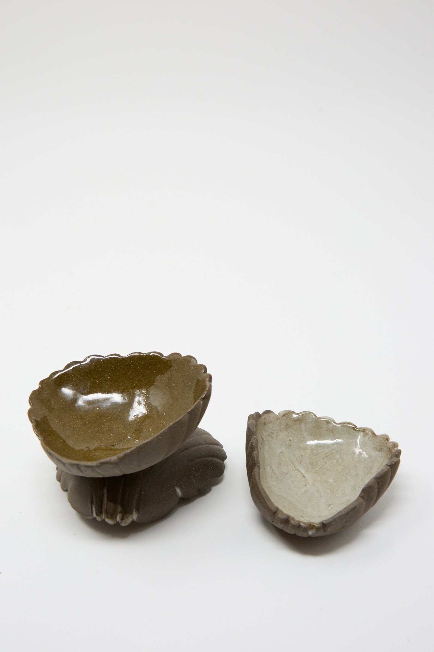 A pair of Lost Quarry's Small Ceramic Shell Dishes in brown with a light glaze sits gracefully on a white surface, showcasing their scalloped, shell-shaped edges.