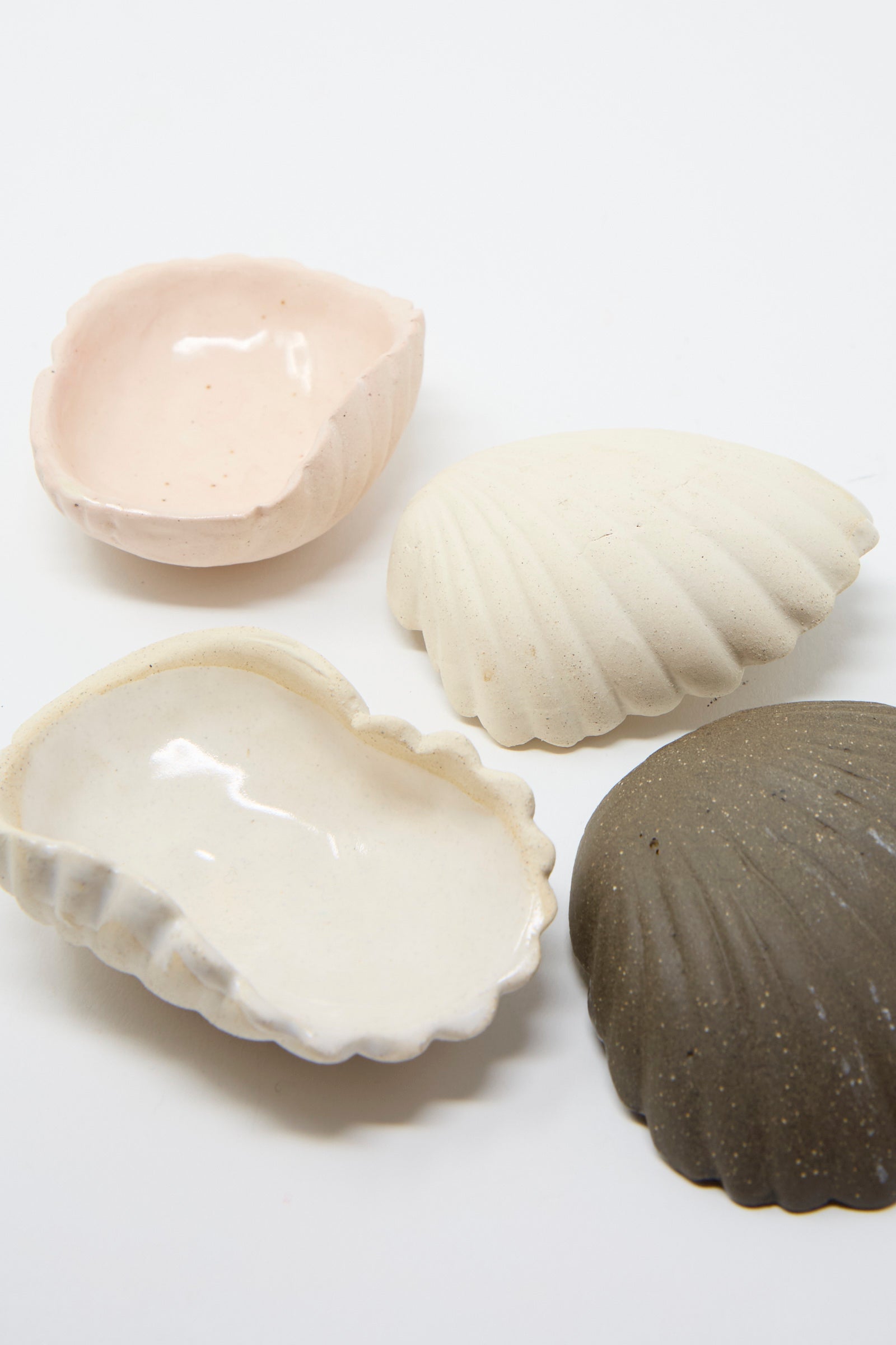 Displayed on a white background are four Small Ceramic Shell Dishes in Cream, each  crafted from clay by Lost Quarry. 