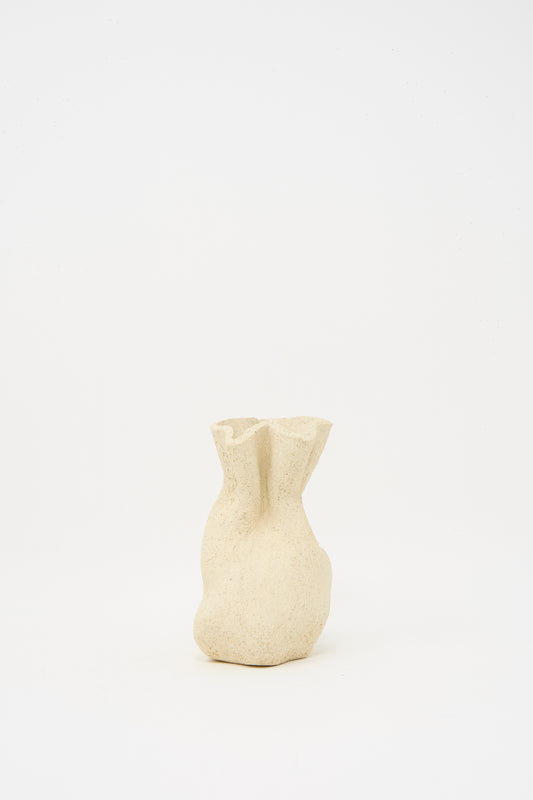 The Textured Clay Folded Vessel II by Lost Quarry is a small, beige ceramic vase with an organic, folded shape and textured finish—handmade to showcase unique floral arrangements against a simple white background.