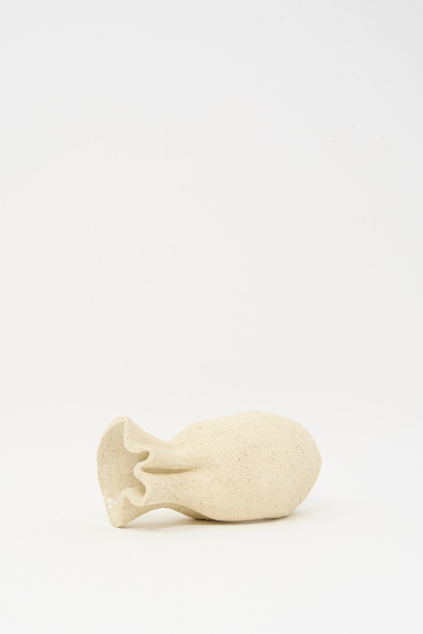 The Lost Quarry Textured Clay Folded Vessel III is a handmade, off-white ceramic piece with a ruffled opening, shown lying horizontally on a plain white background.